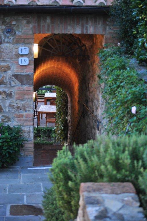 A stone archway leading to a garden with tables and chairs.