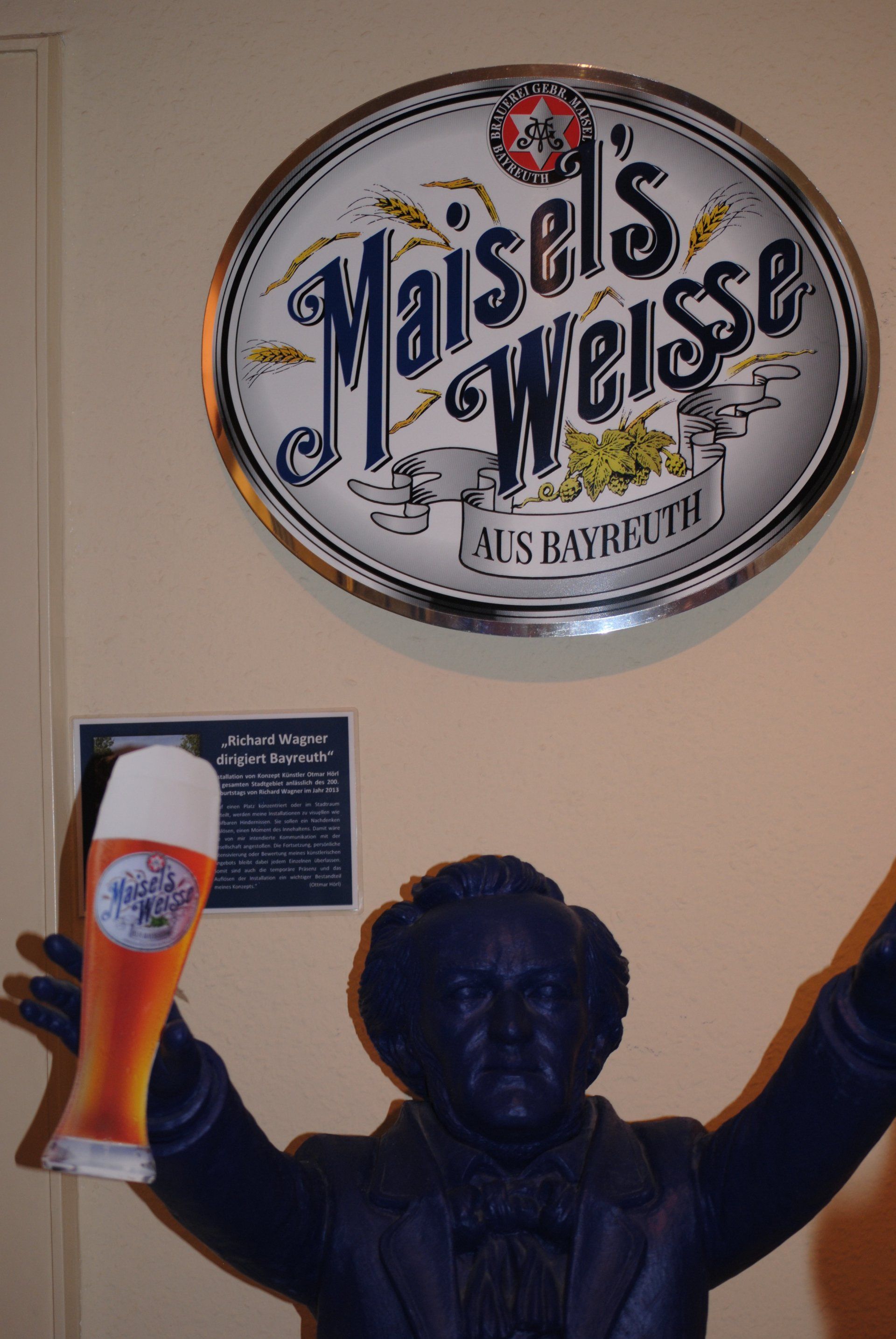 A statue of a man holding a glass of beer under a sign that says maisels weisse