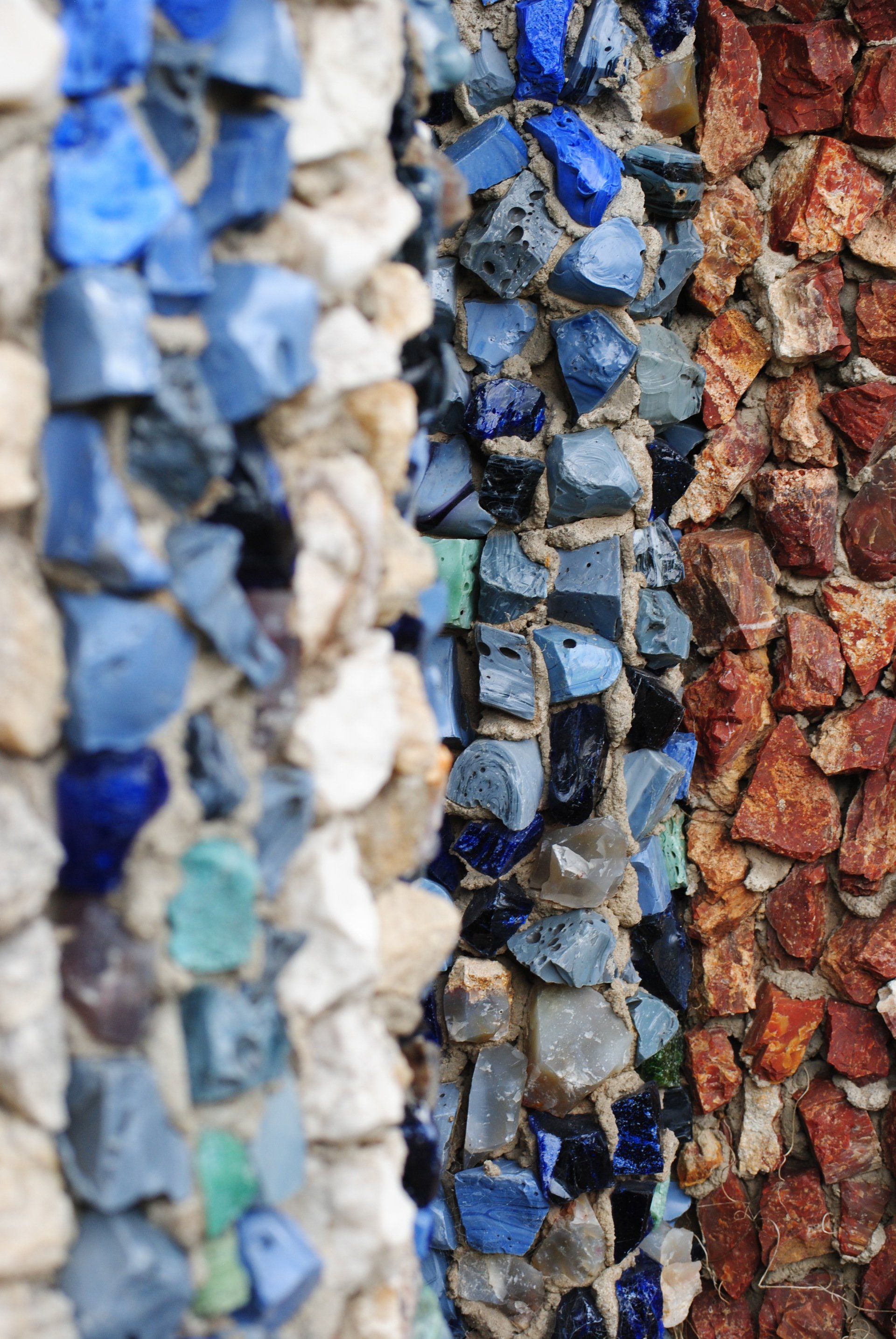 A close up of a stone wall with blue , white and red rocks.