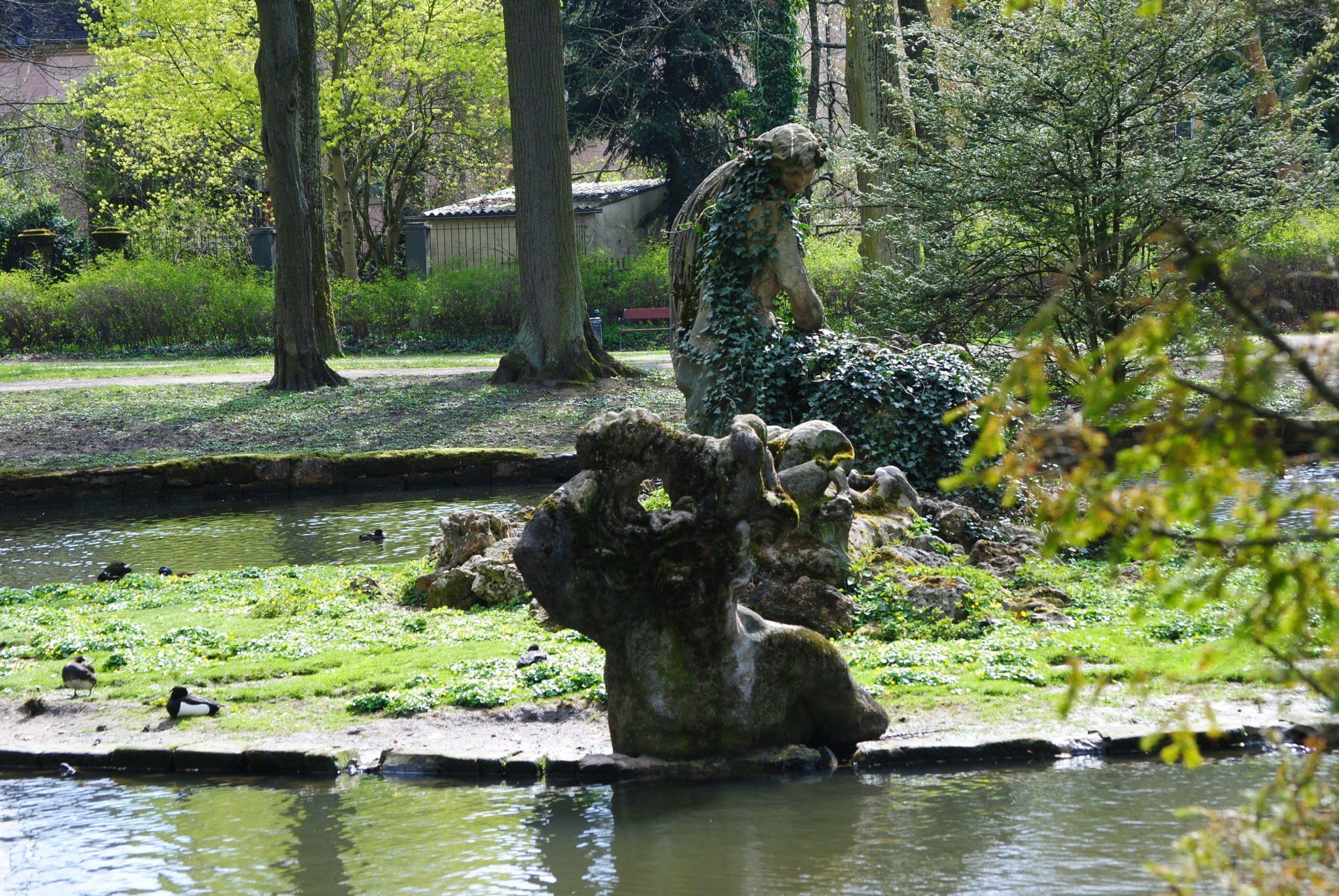 A statue of a woman standing in a pond in a park.