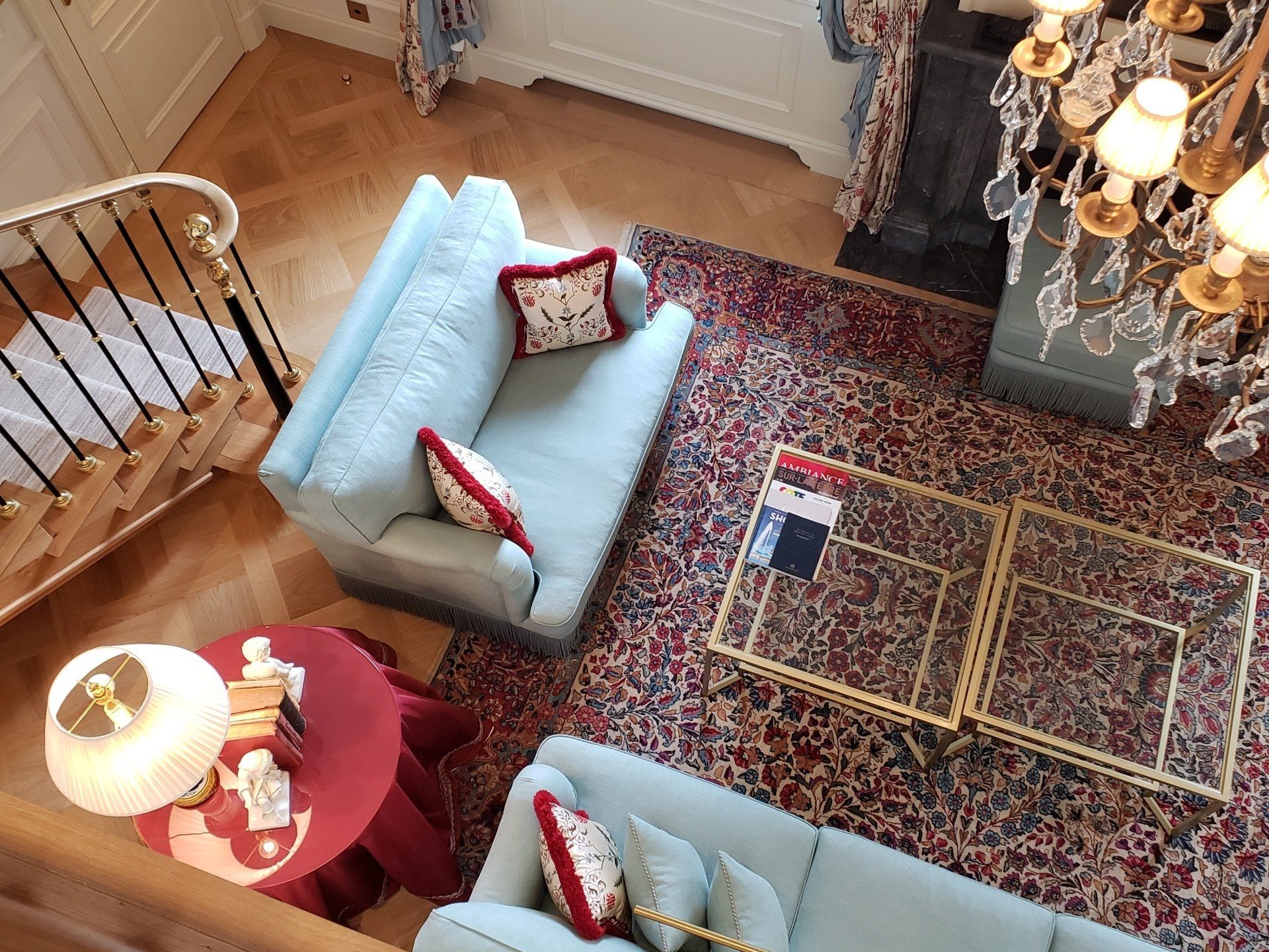 An aerial view of a living room with a couch , chair , table and chandelier.