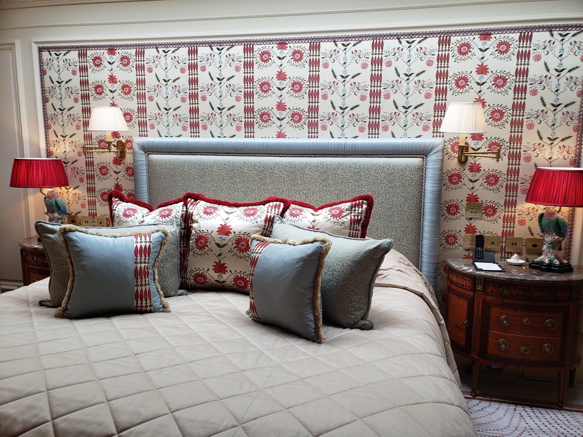 A bedroom with a bed , nightstands , lamps and a floral wallpaper.