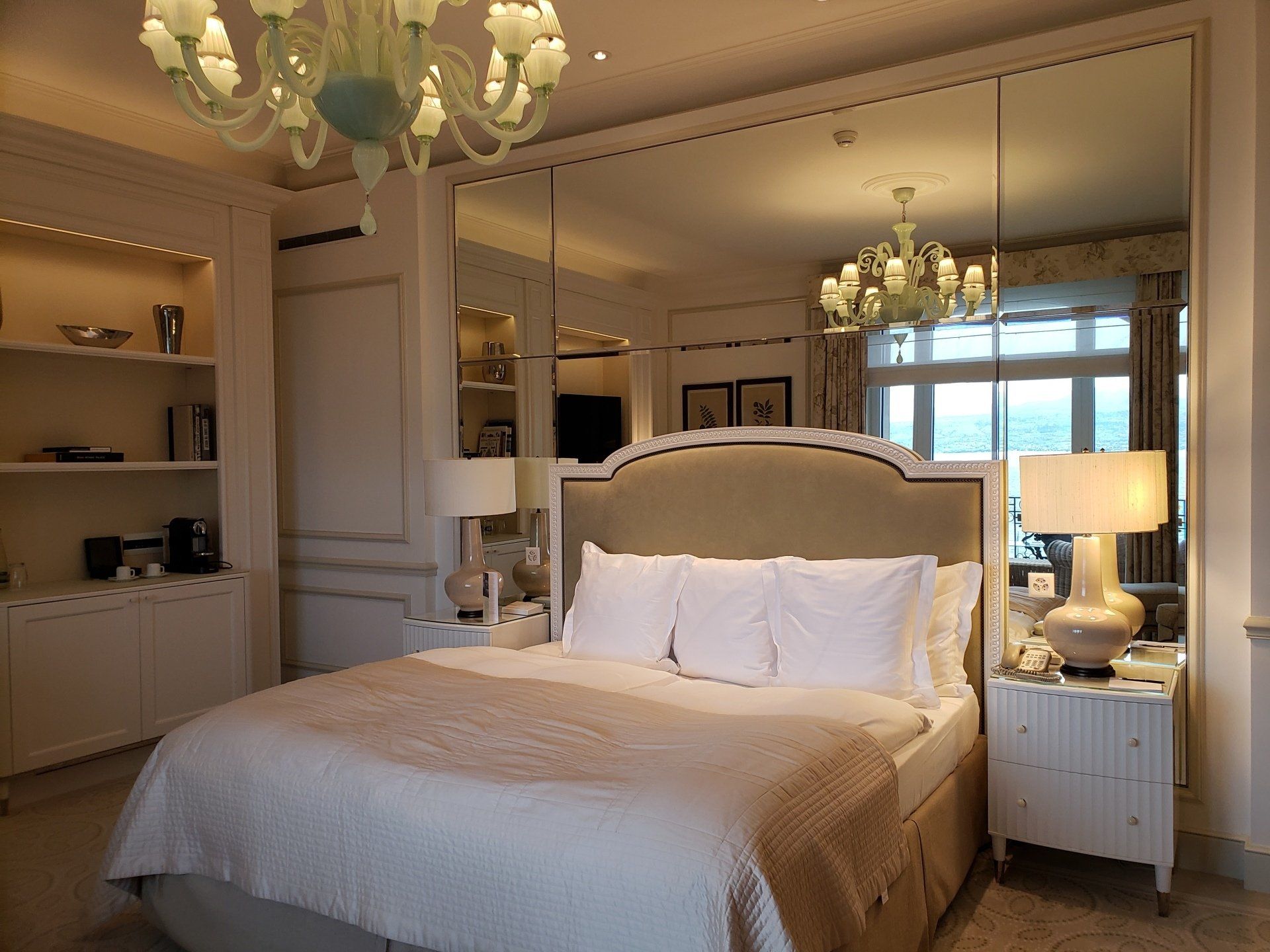 A bedroom with a large bed , nightstands , lamps and mirrors.