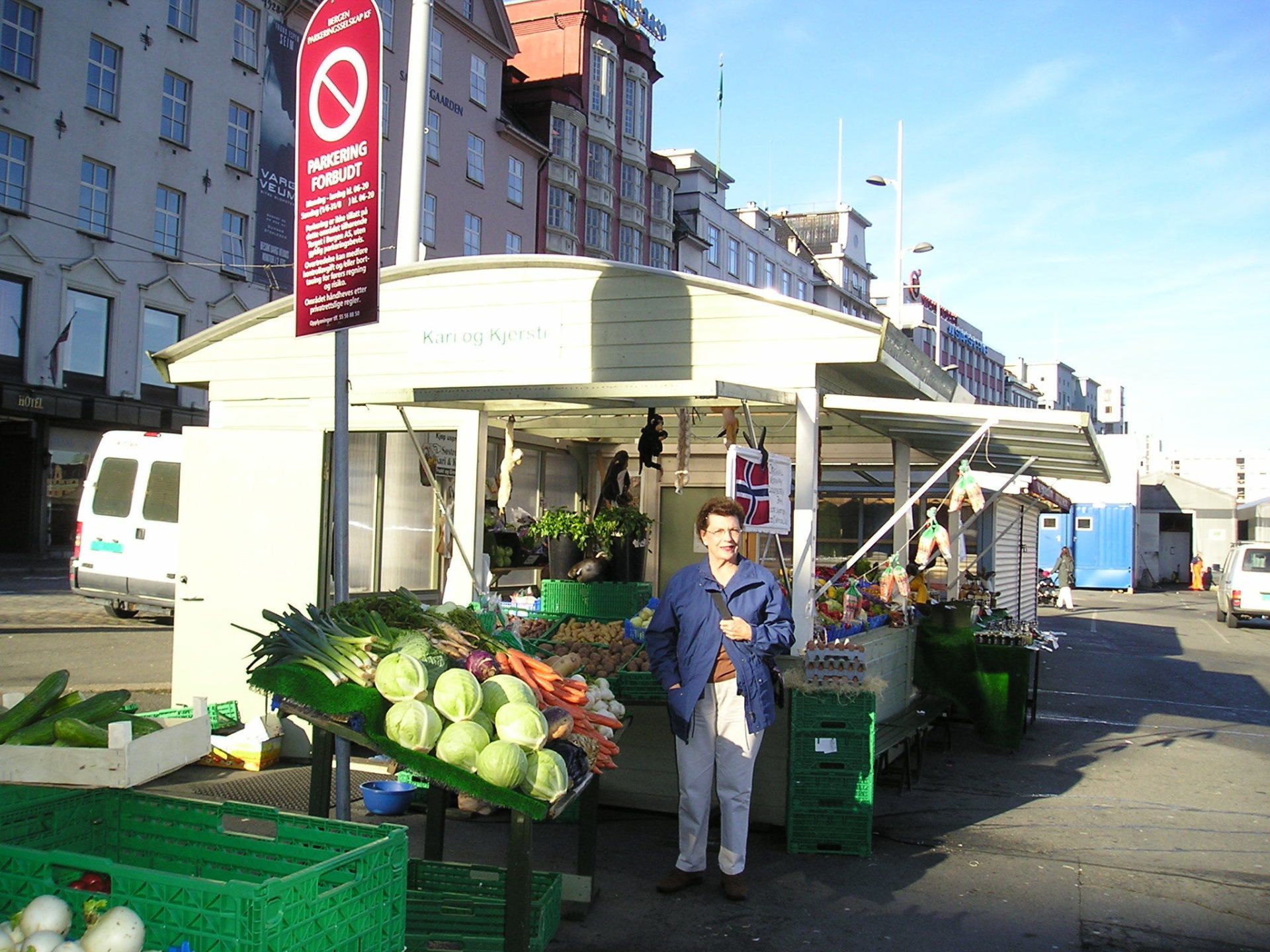 A man stands in front of a vegetable stand with a sign that says no parking