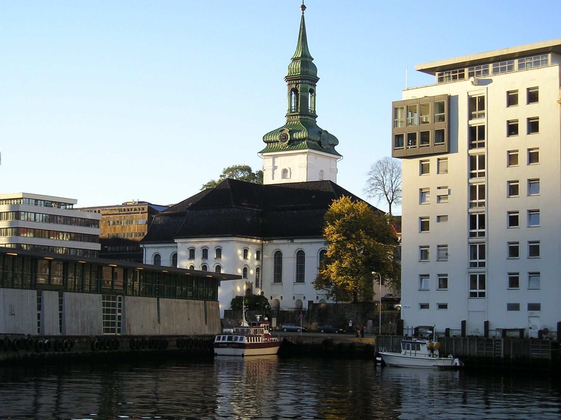 A white building with a green steeple is next to a body of water