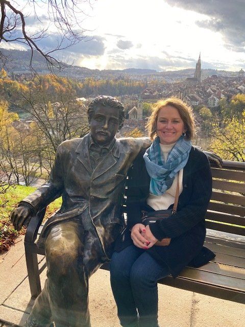 A woman is sitting on a bench next to a statue of a man