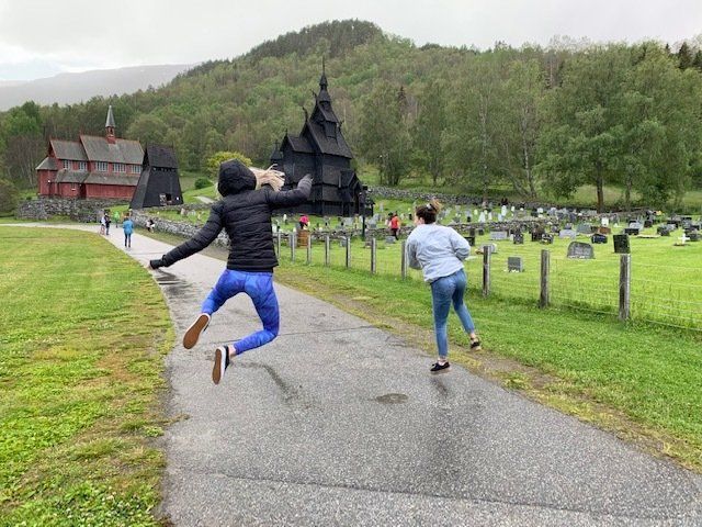 Two people are jumping in the air on a path in front of a cemetery.
