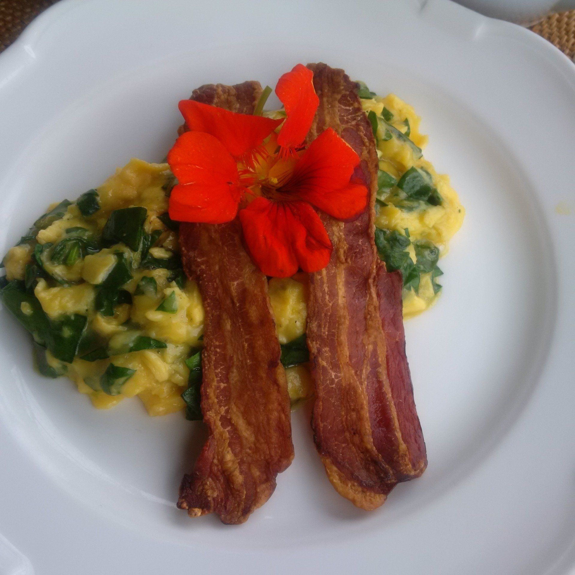 A white plate topped with bacon scrambled eggs and a flower