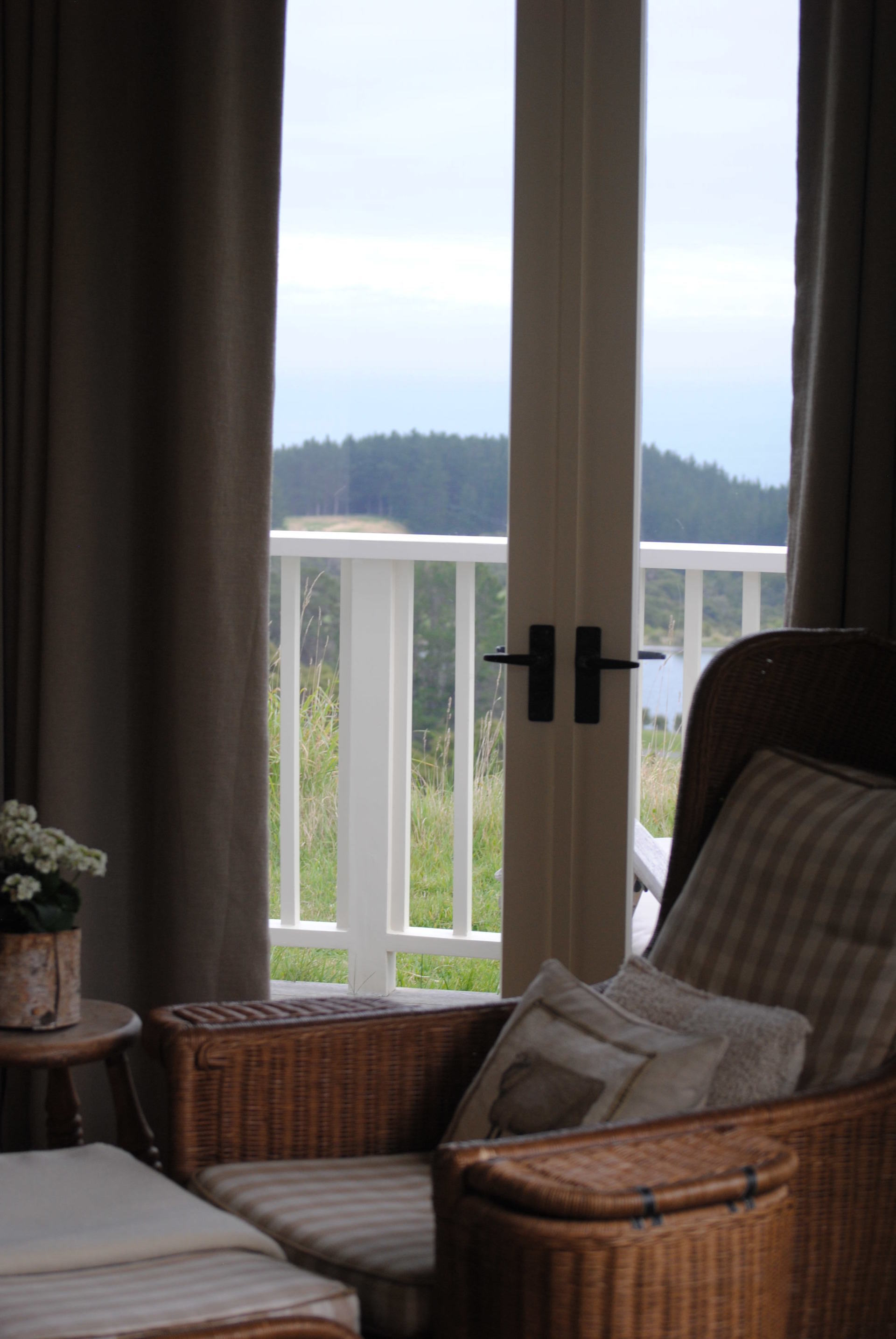 A wicker chair is sitting in front of a window with a view of a balcony.