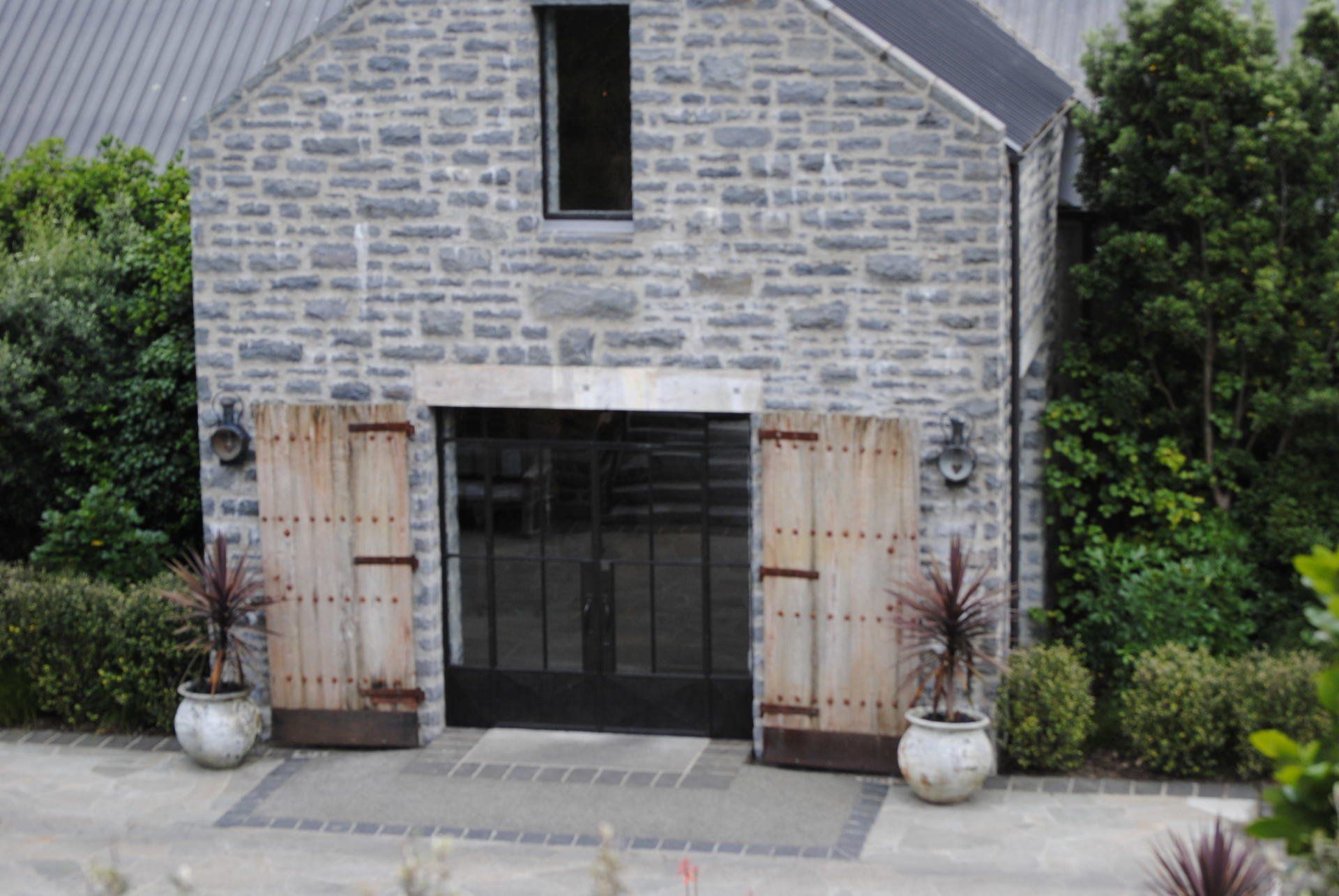 A large stone building with wooden doors and potted plants in front of it.