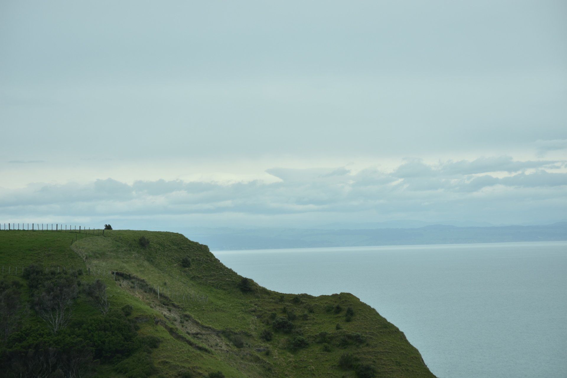 A person is standing on top of a cliff overlooking the ocean.