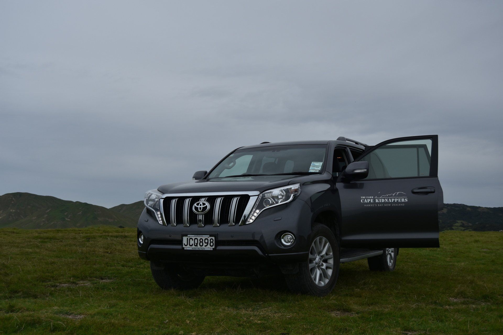 A black suv is parked in a grassy field with its doors open.
