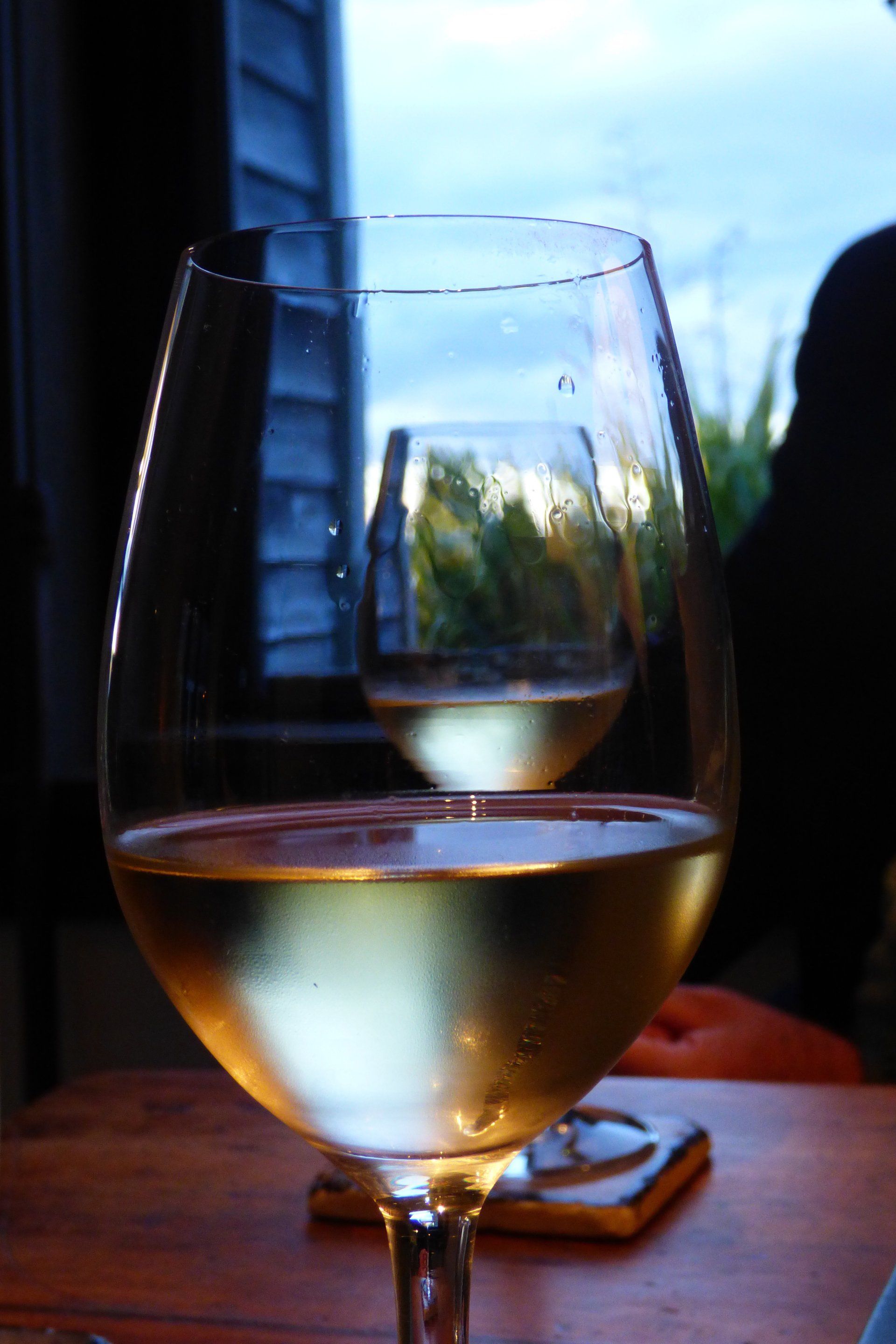 A glass of wine sits on a table in front of a window
