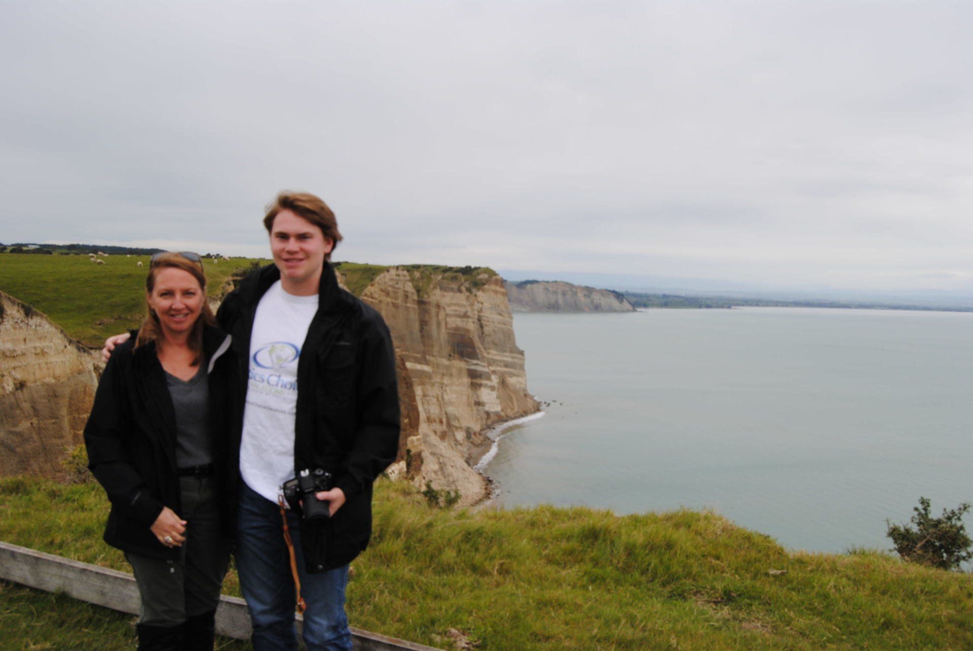 A man and a woman are standing on a cliff overlooking a body of water.