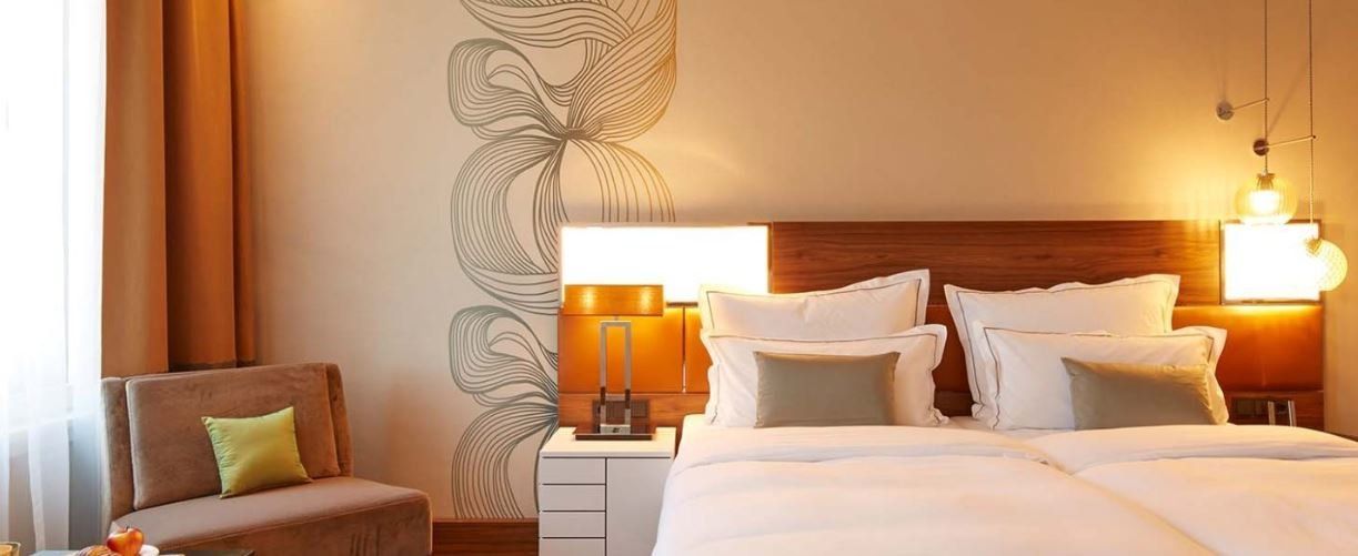 A hotel room with a bed , chair , nightstand and lamp.