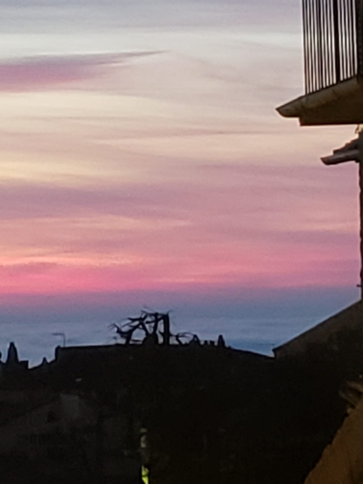 A sunset over a city with a balcony in the foreground.