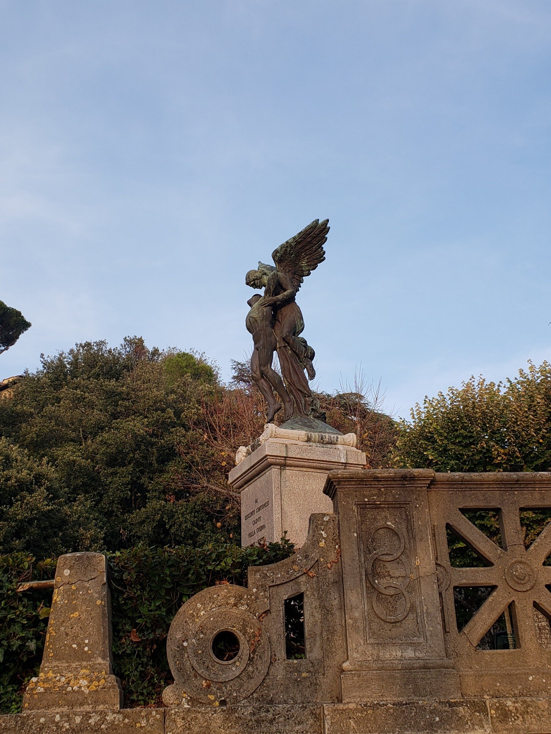 A statue of a man with wings standing on top of a stone wall.