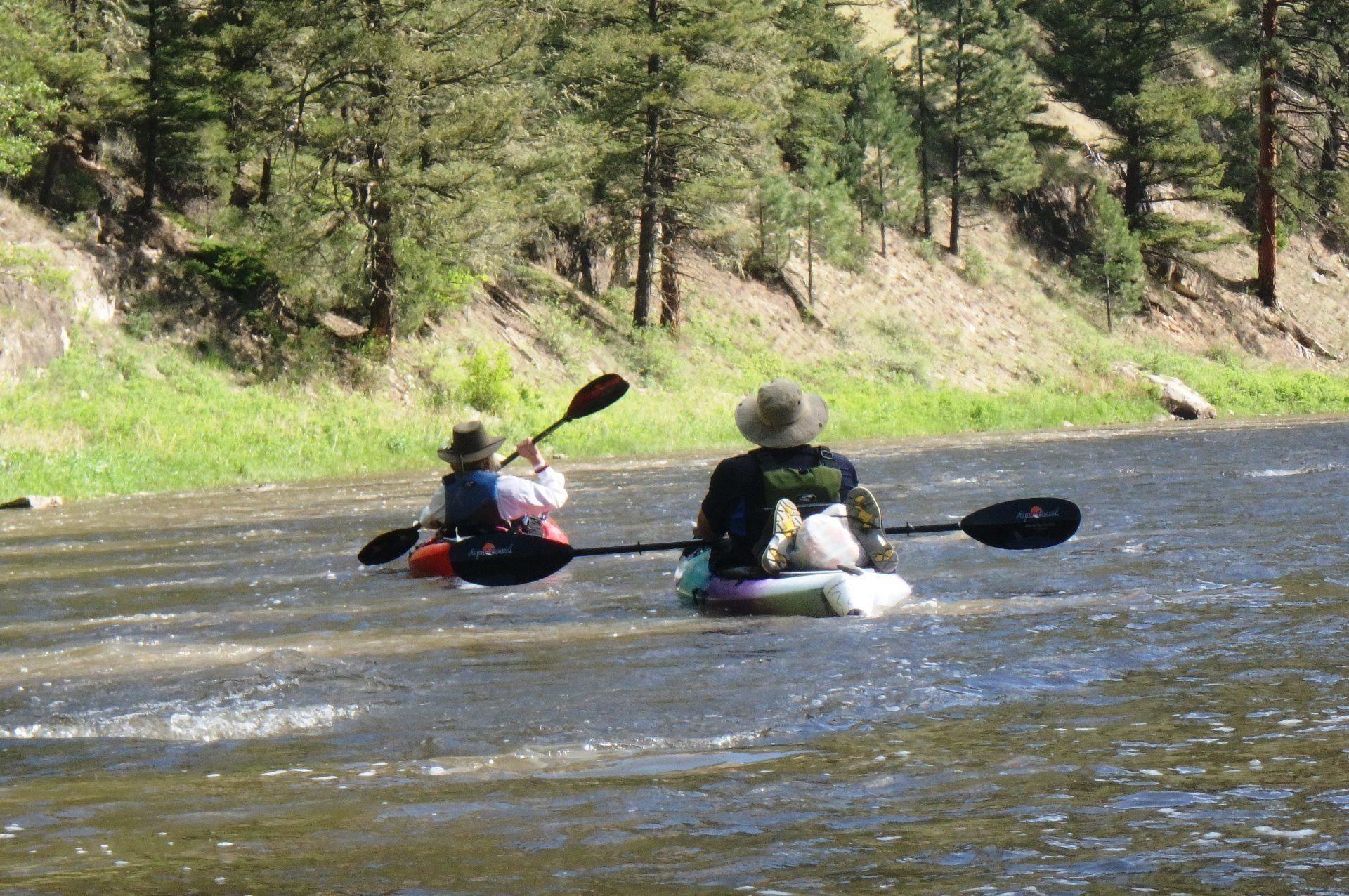Two people are paddling kayaks down a river.
