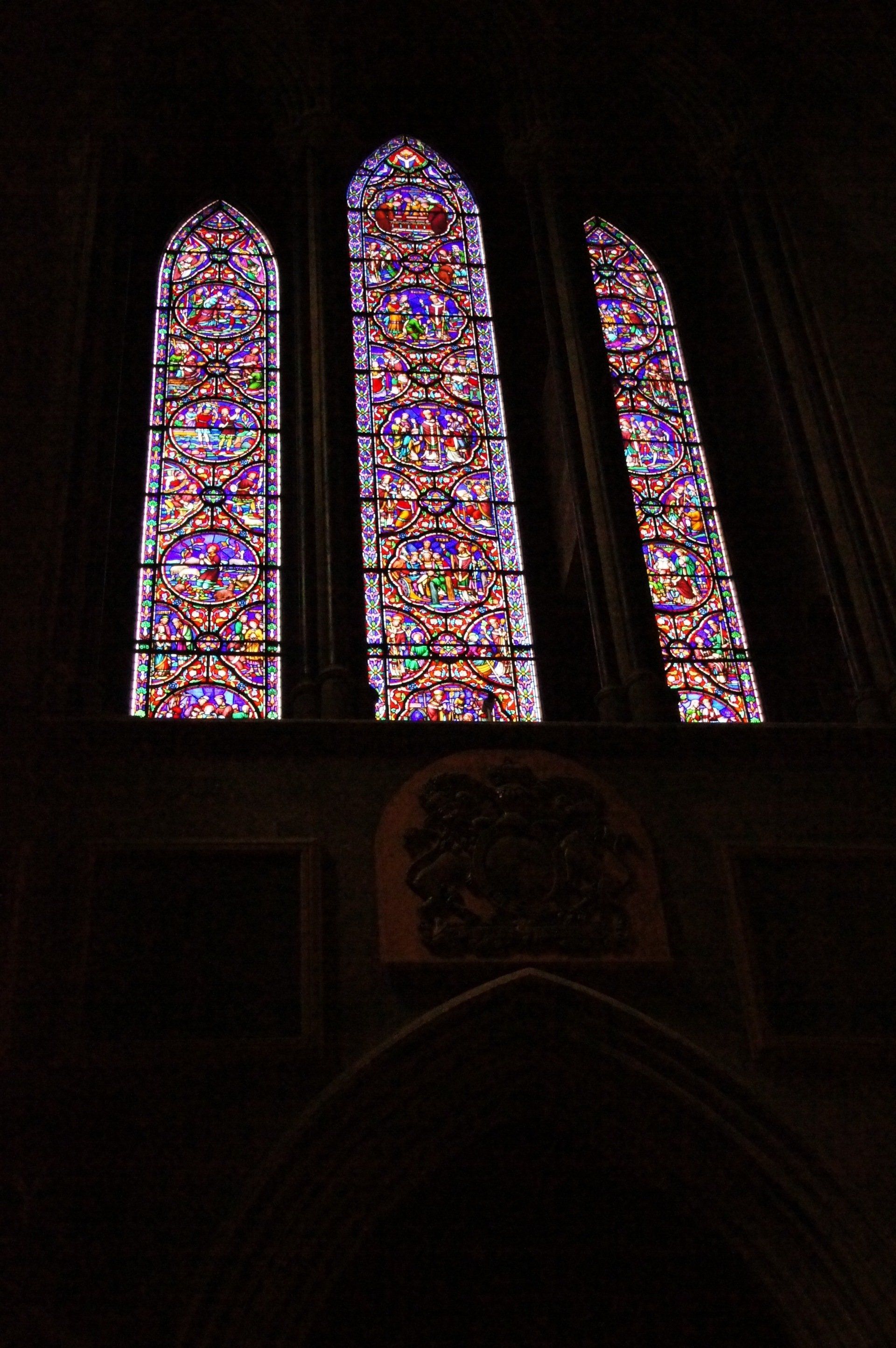 Three stained glass windows in a church with a dark background