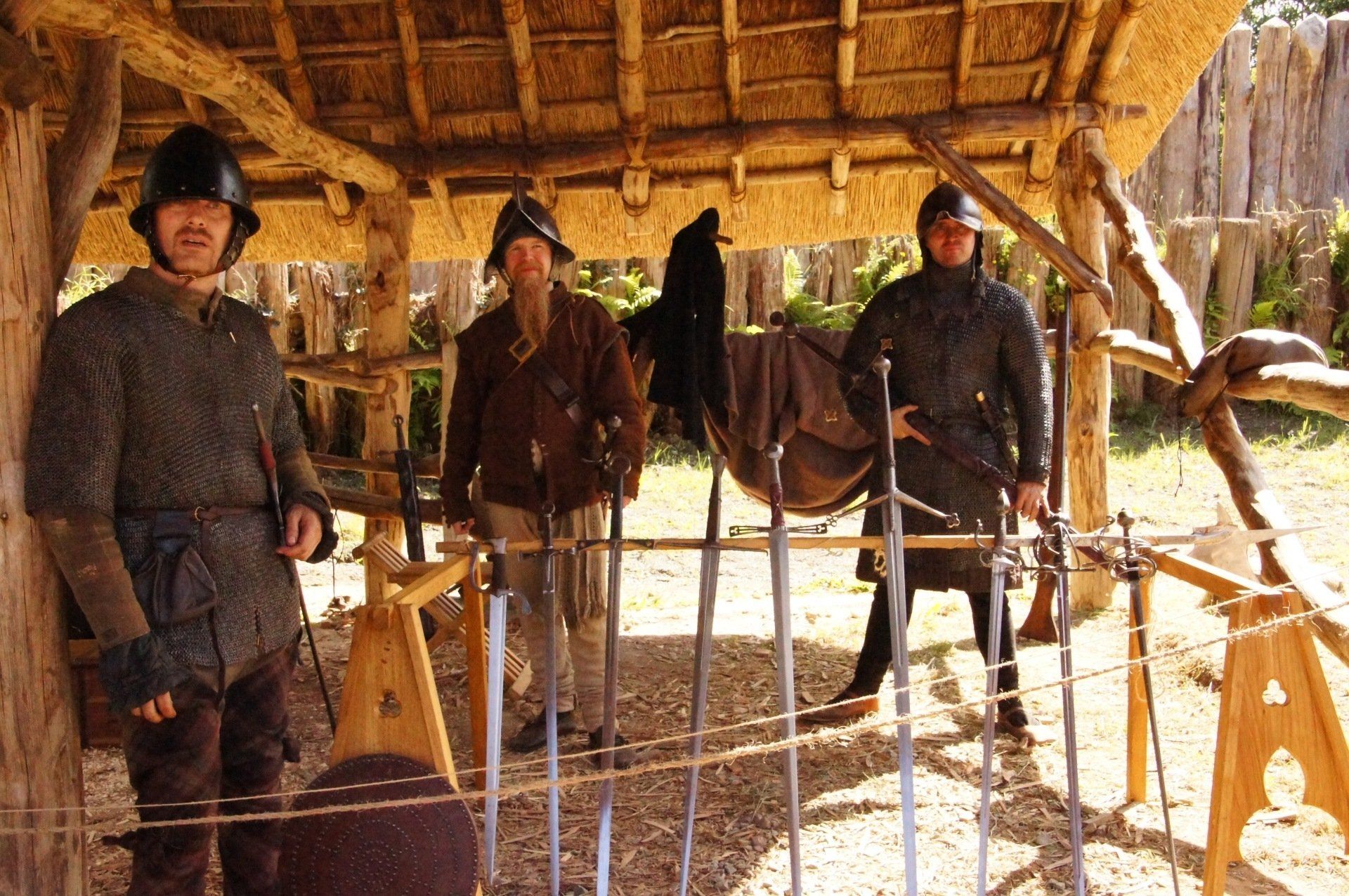 A group of men are standing under a thatched roof holding swords