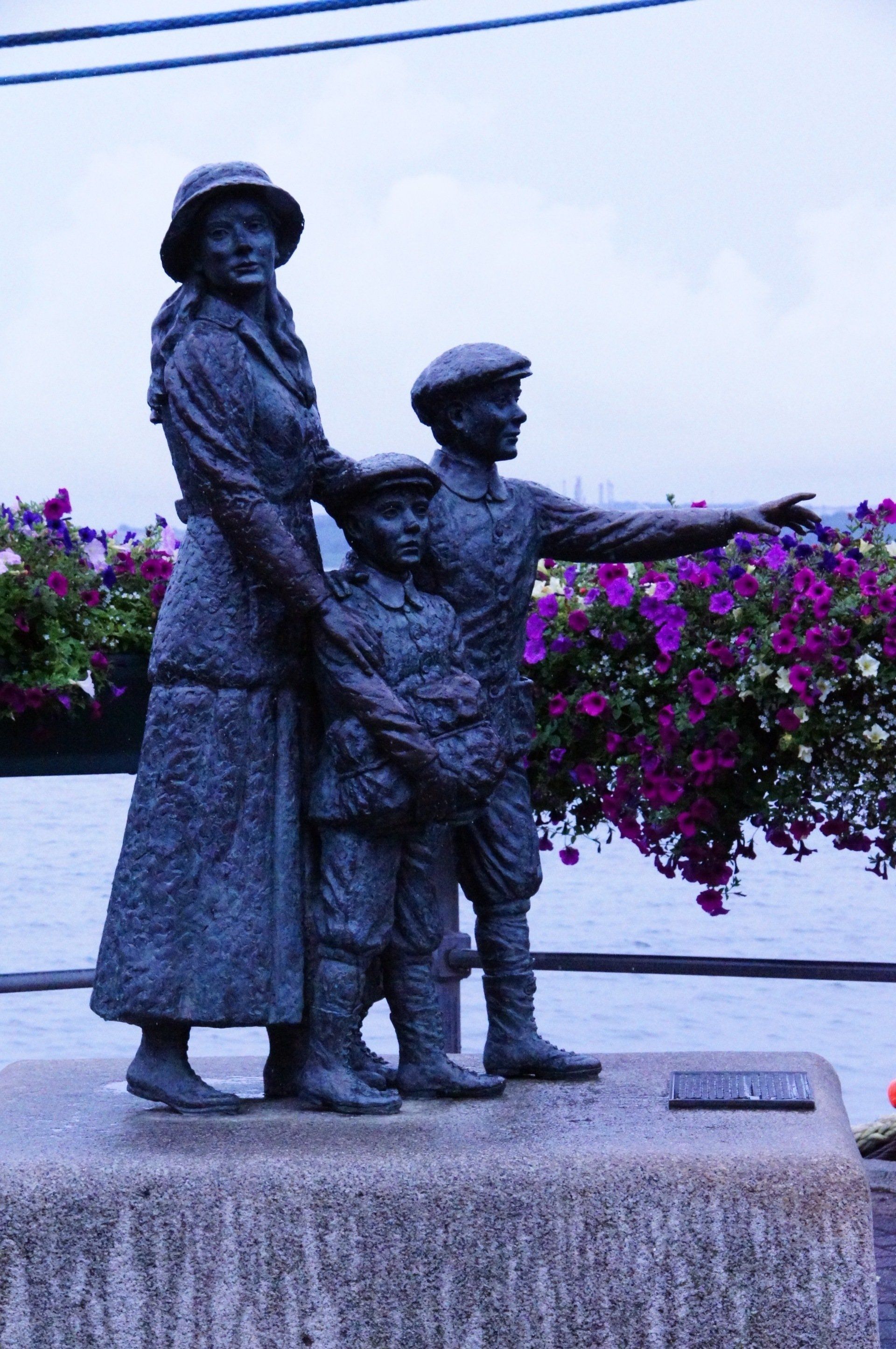 A statue of a woman and two children with purple flowers in the background