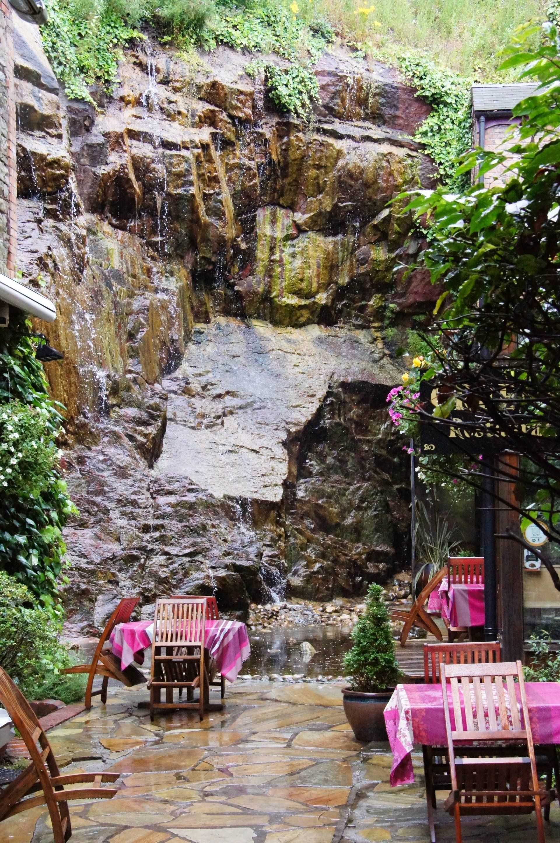 There is a waterfall in the background and tables and chairs in front of it.