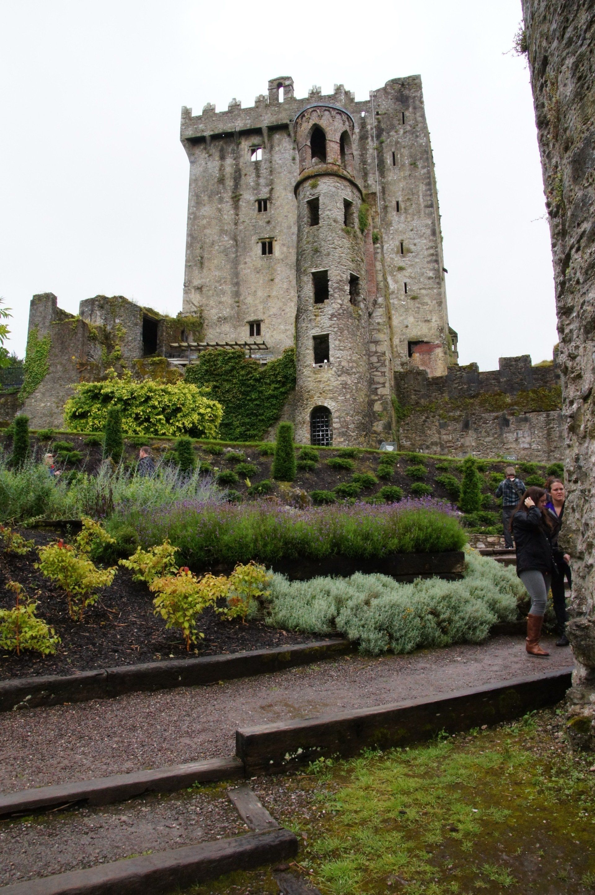 A woman is standing in front of a castle in a garden.