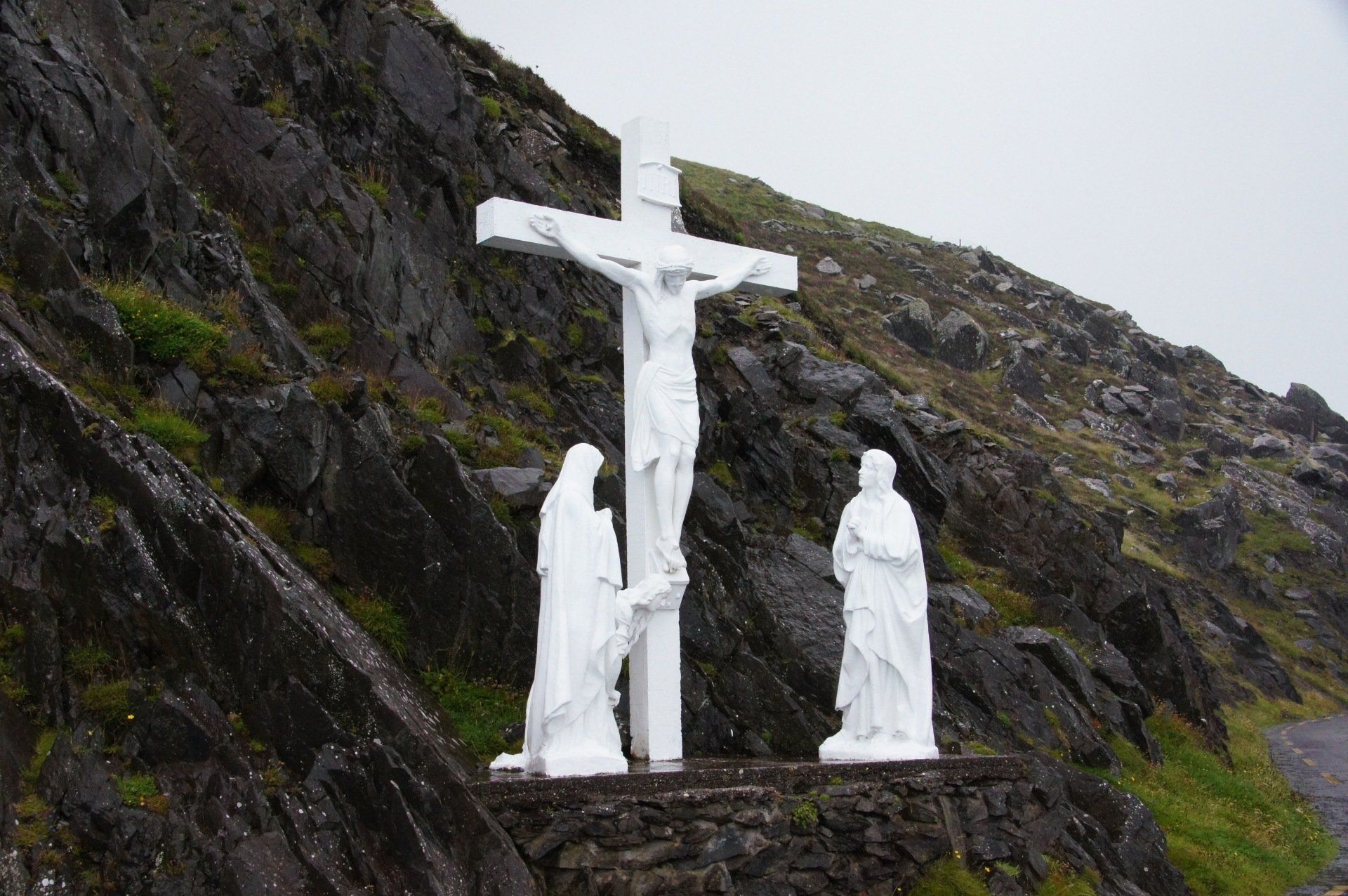 A statue of jesus on a cross with two statues of people standing next to it.