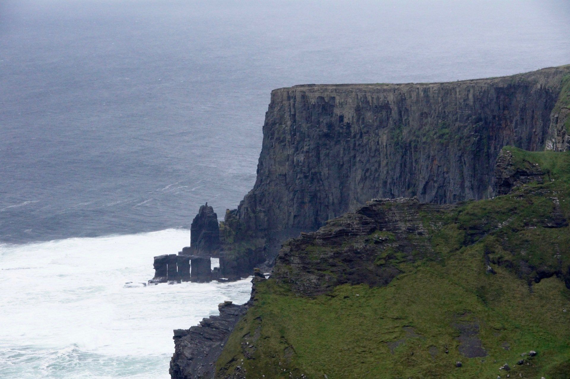A cliff overlooking the ocean with waves crashing on it.