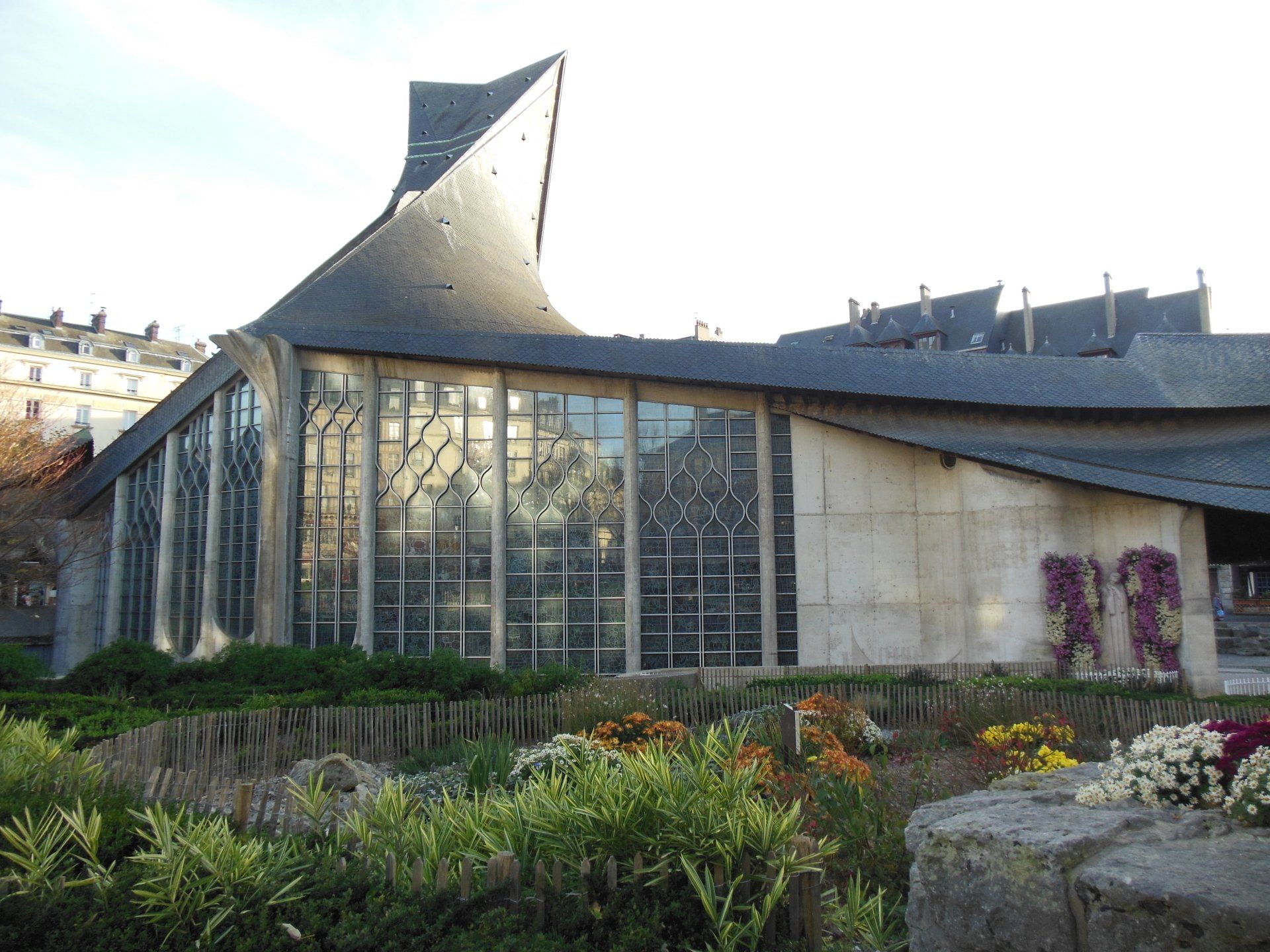 A large building with a lot of windows is surrounded by bushes and flowers.