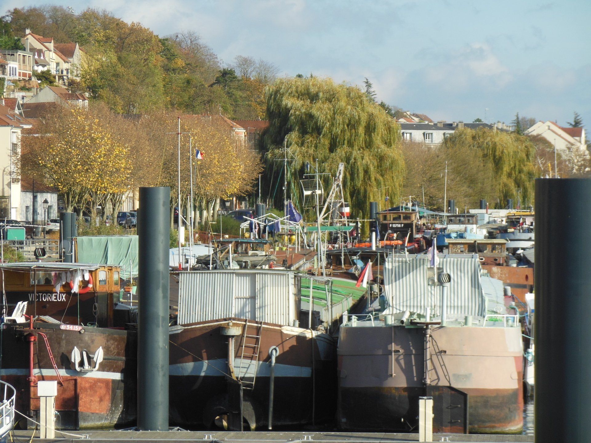 A row of boats are docked in a harbor with trees in the background