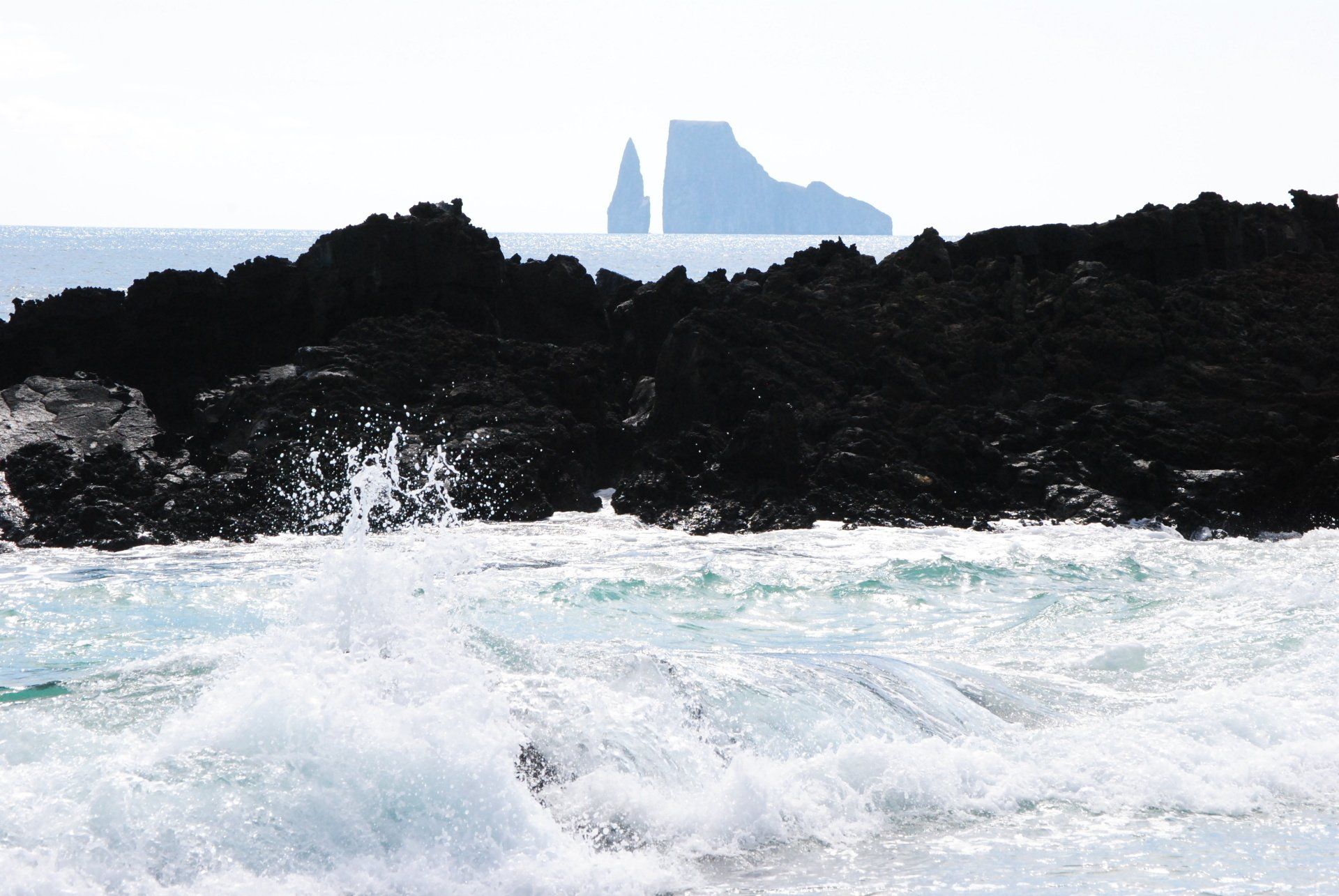 Waves crashing against a rocky shoreline with a mountain in the background
