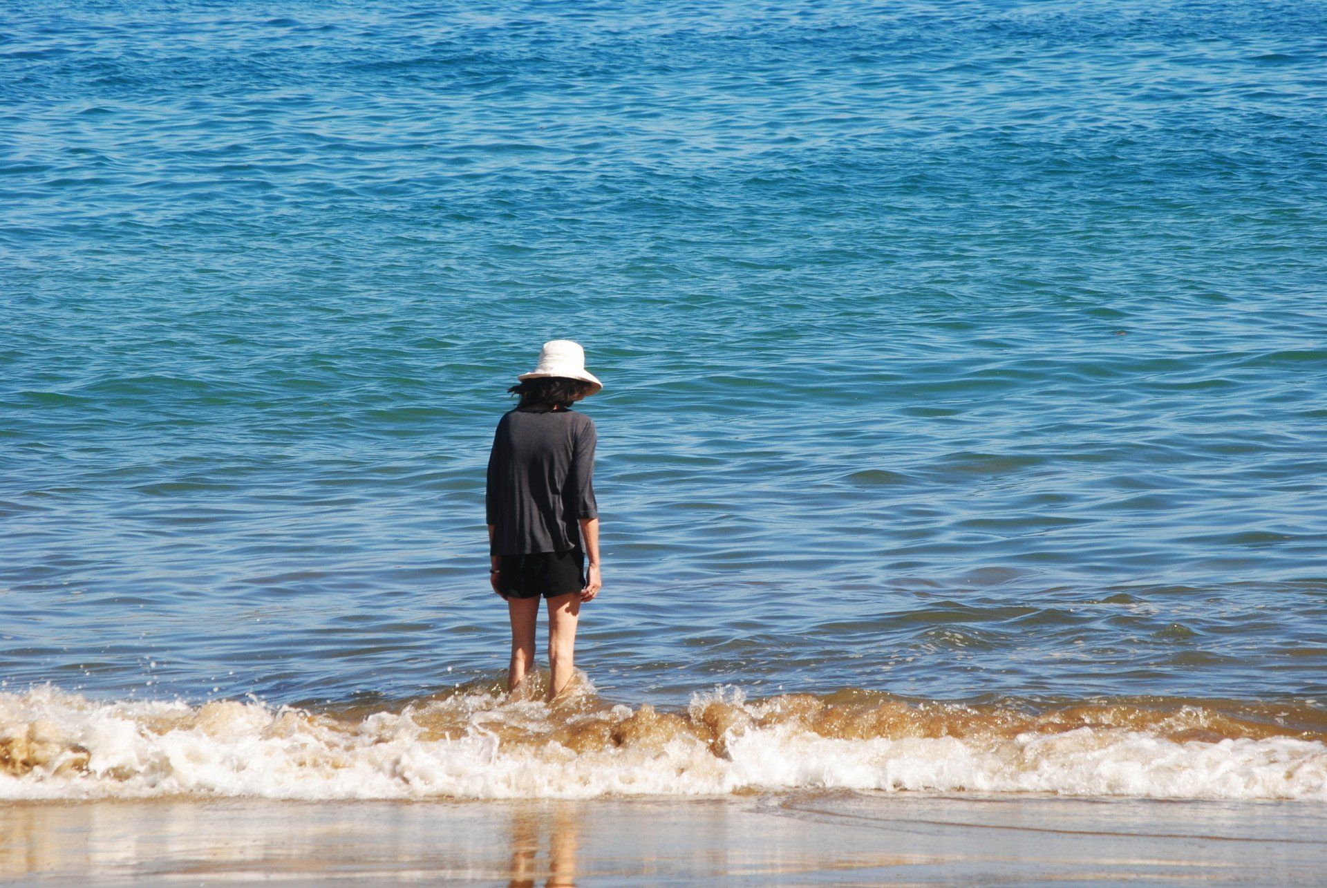 A woman in a hat is standing in the ocean on a beach.