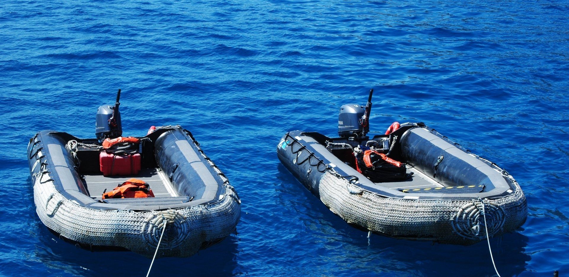 Two boats are tied to each other in the ocean.