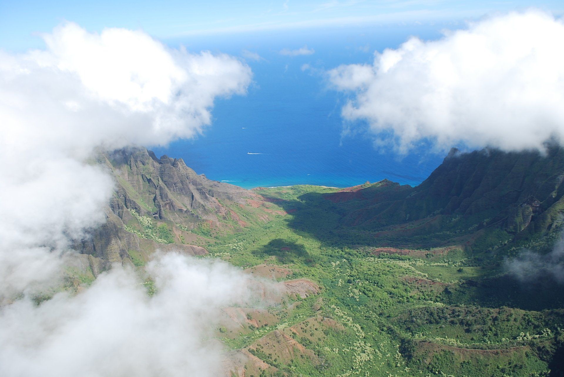 An aerial view of a valley surrounded by mountains and clouds with a body of water in the background.