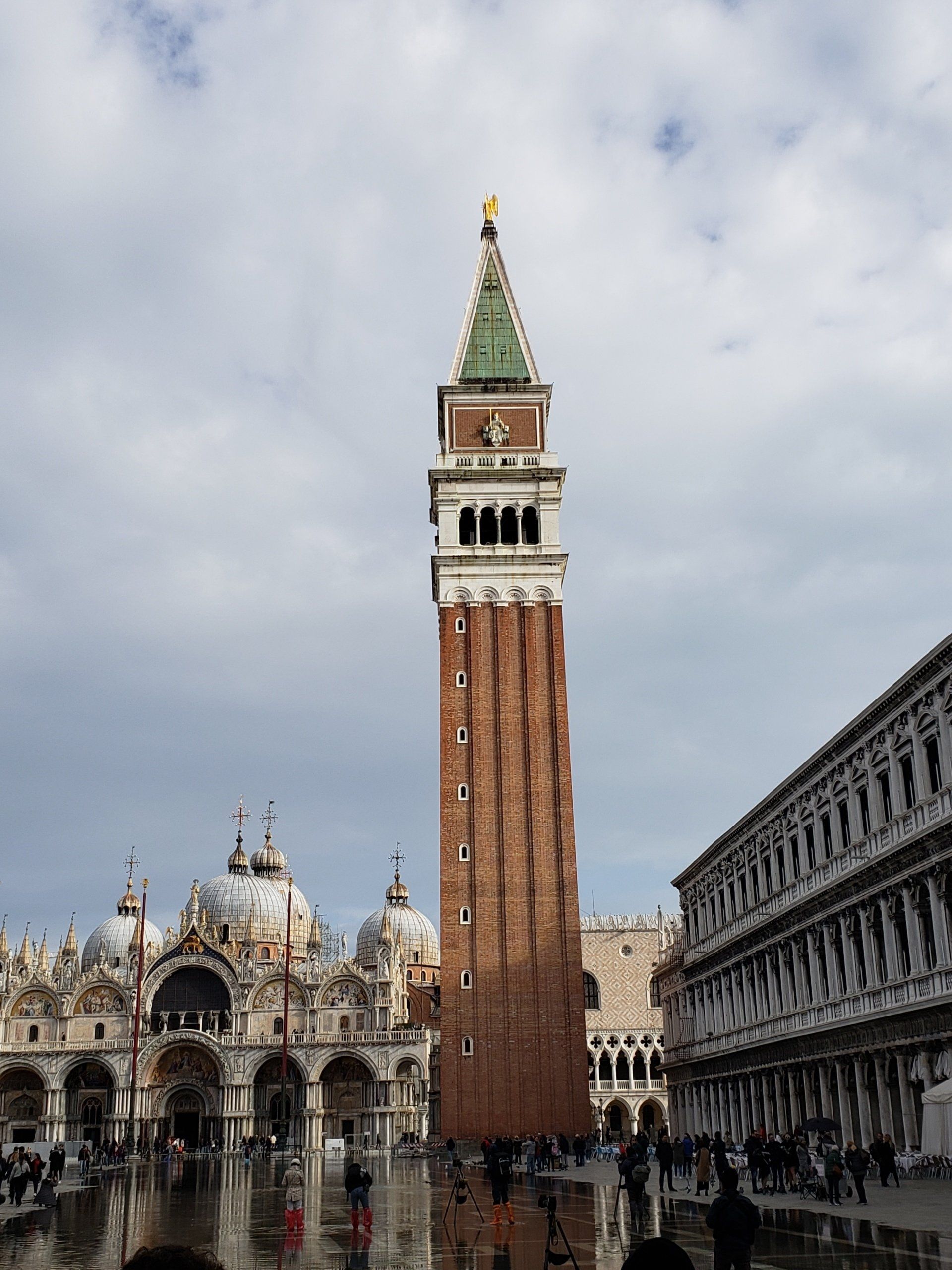 A large brick tower with a green roof is in the middle of a city square.