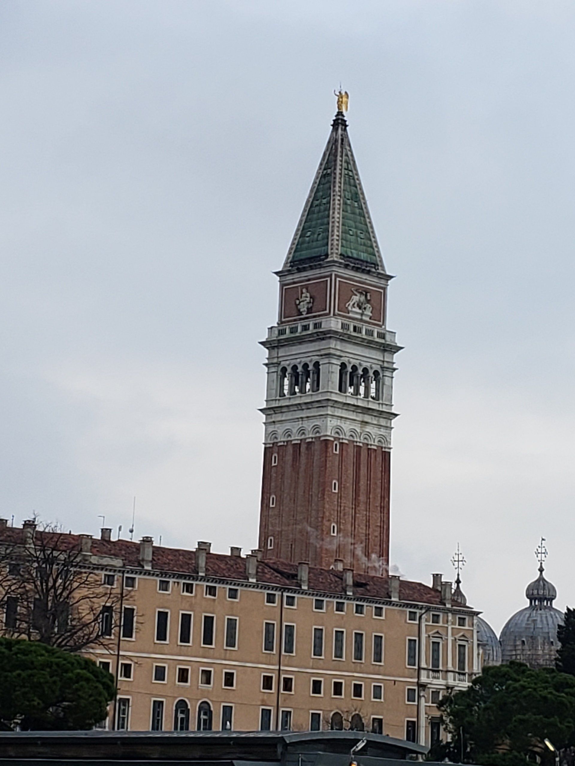A large clock tower with a statue on top of it is in front of a building.
