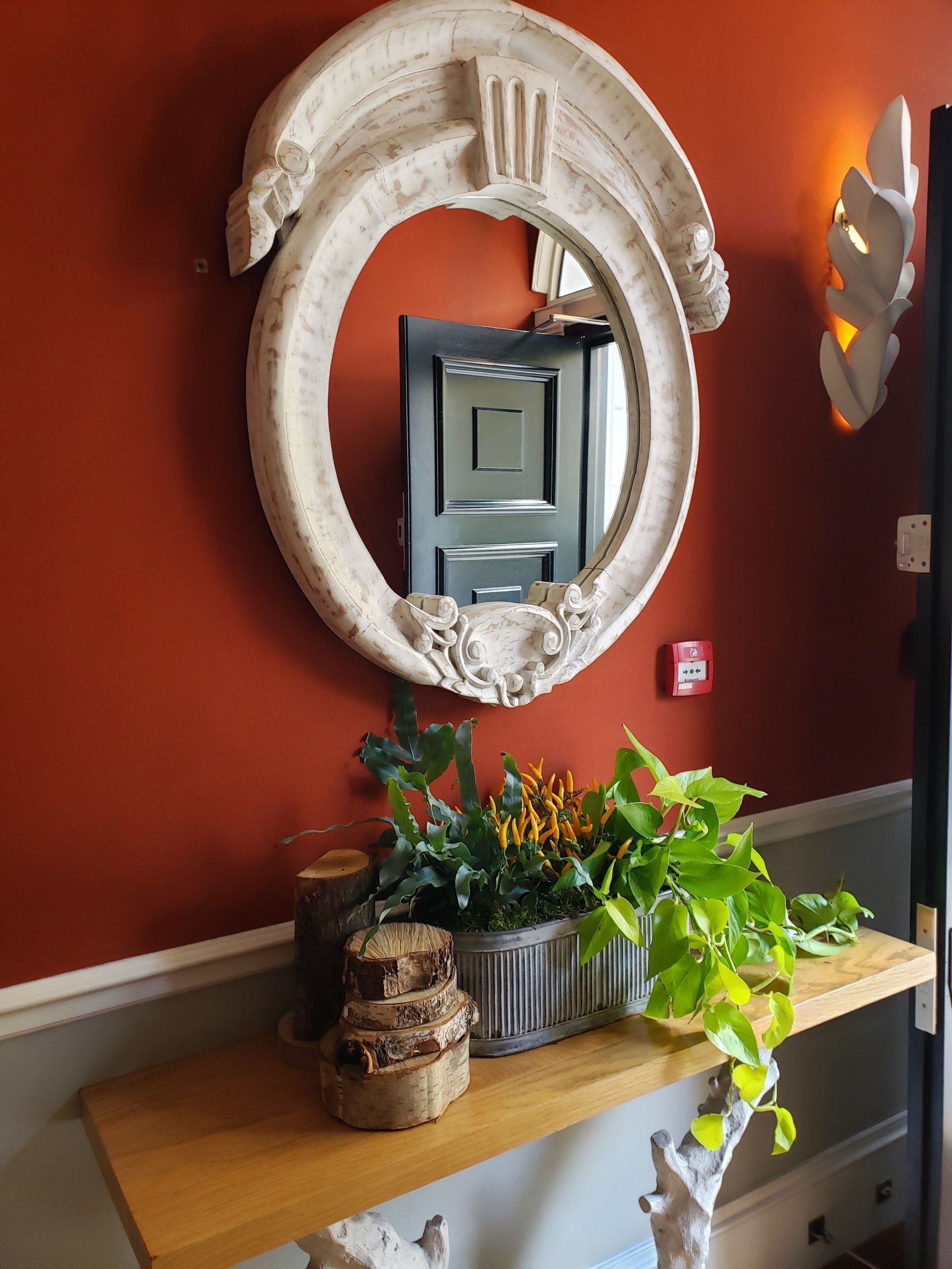 A mirror is hanging on a red wall above a wooden table.