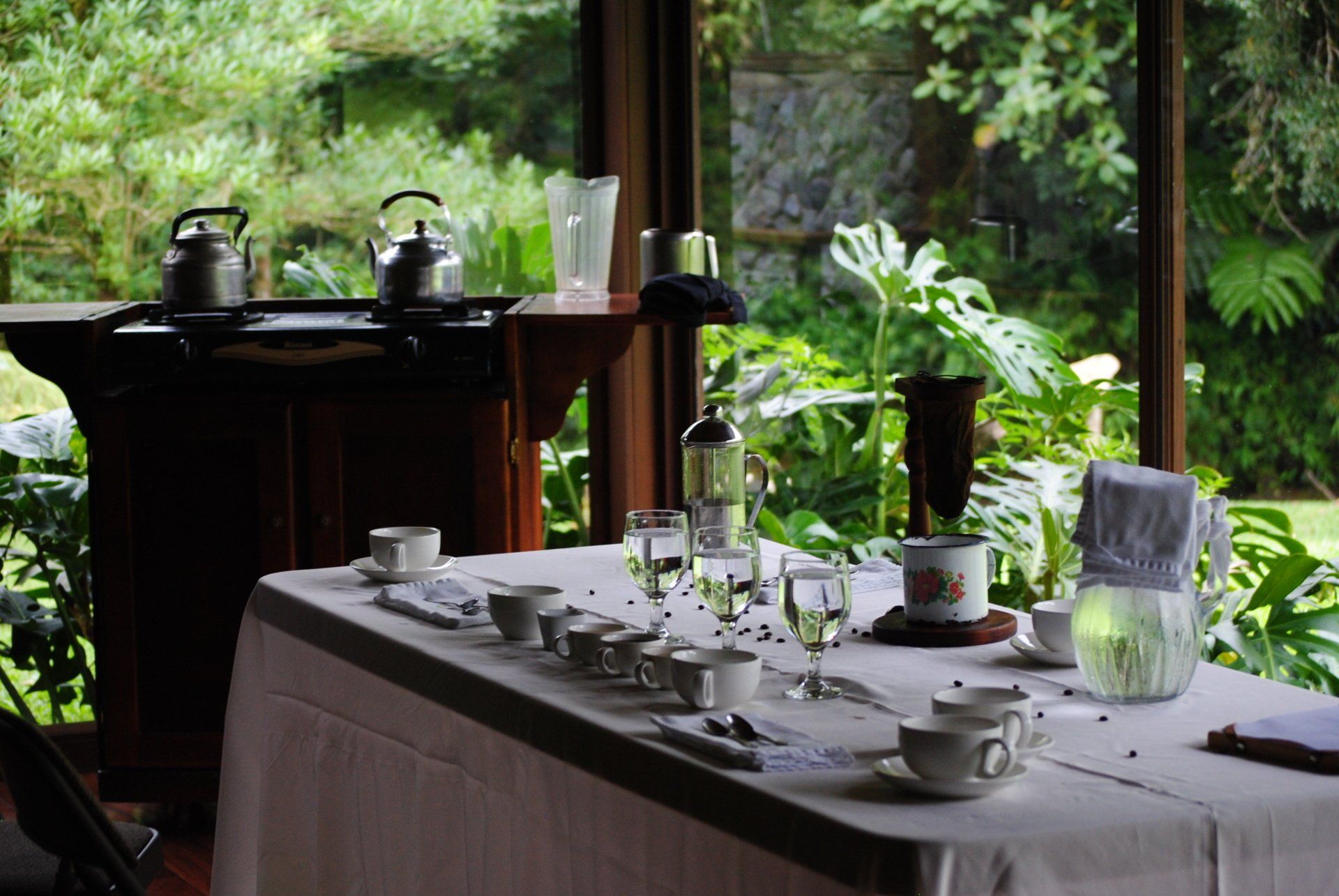 A long table with cups and glasses on it in front of a window