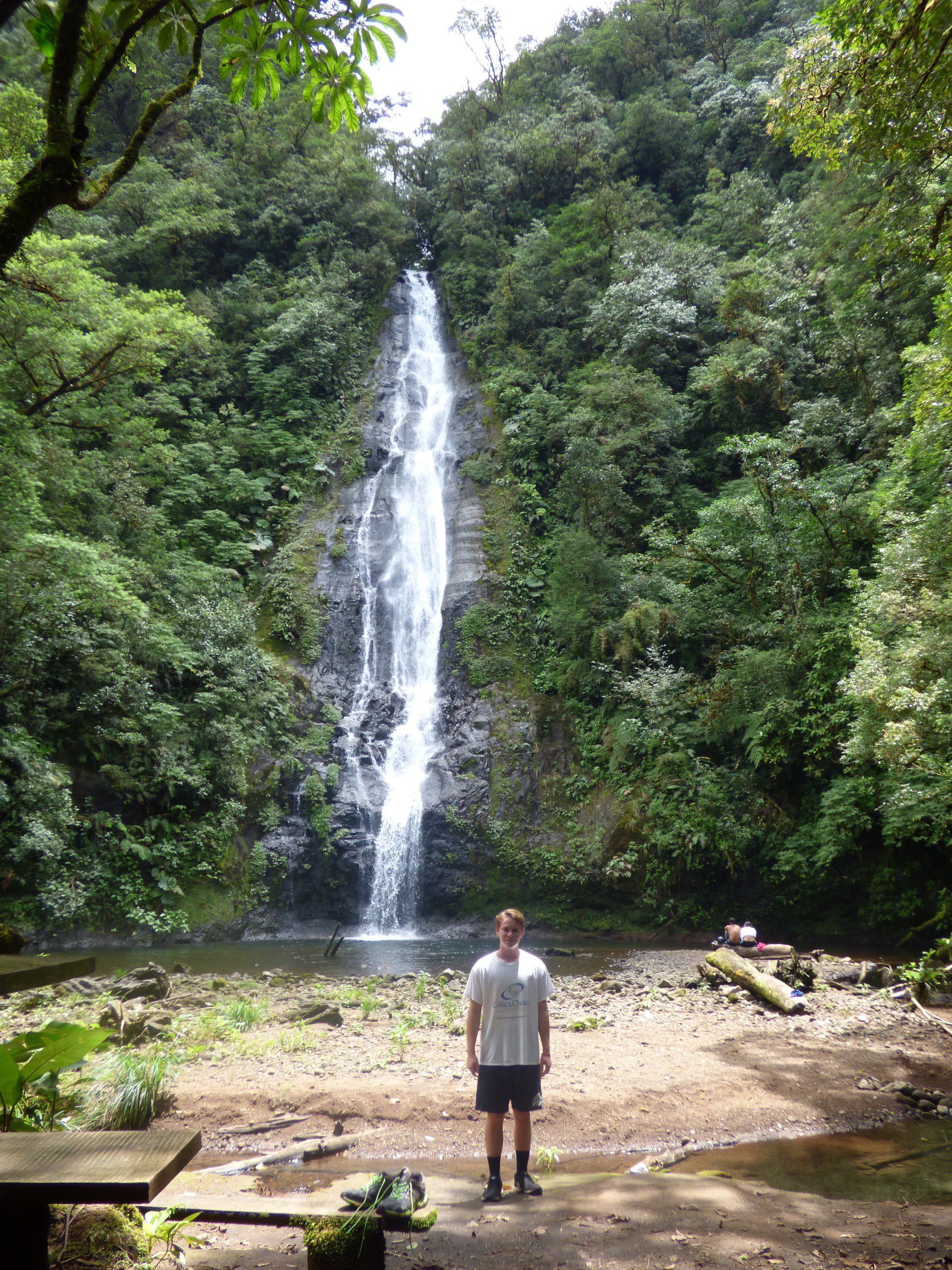 A man is standing in front of a waterfall in the woods.