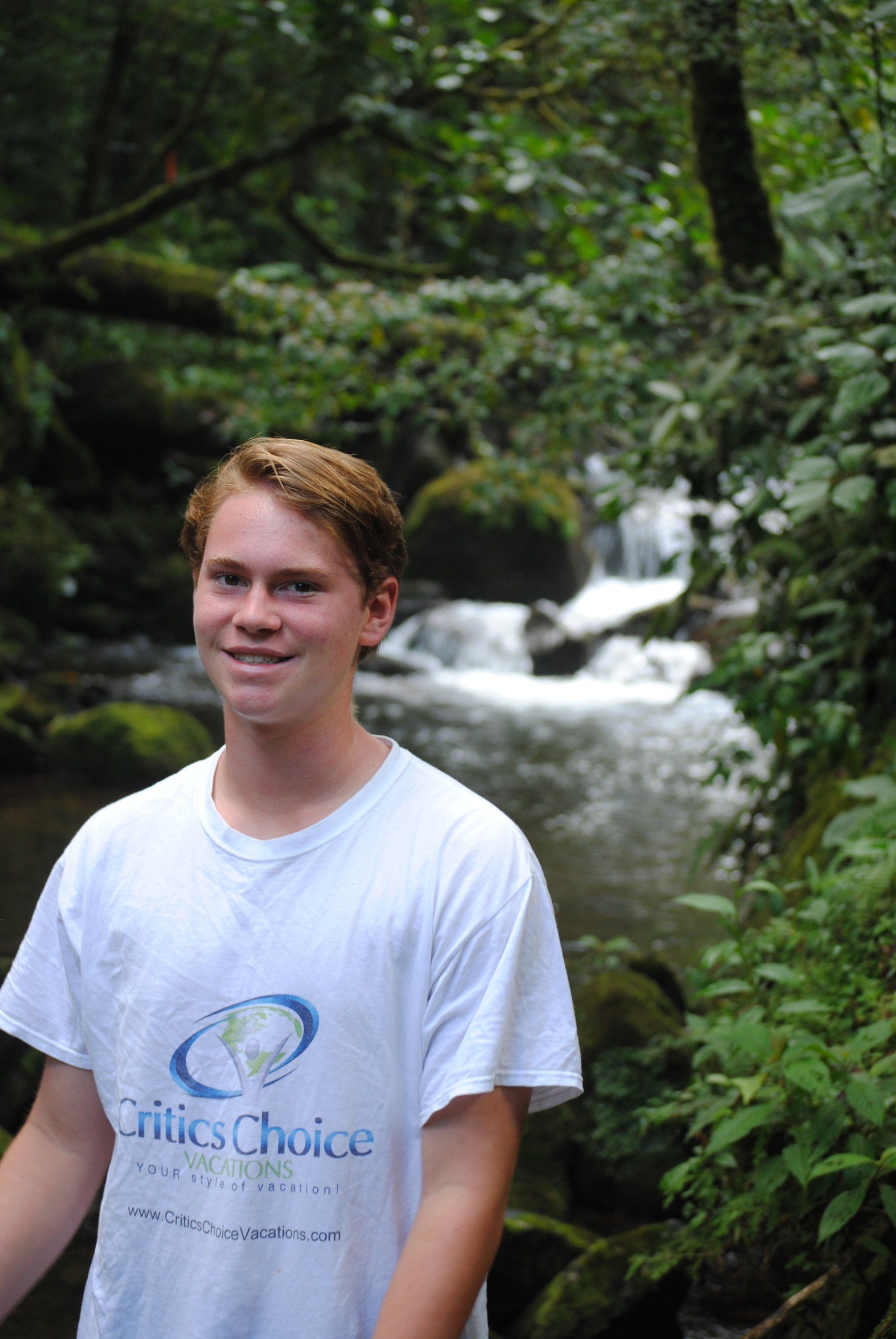 A young man wearing a white t-shirt with the word choice on it is standing in front of a stream.