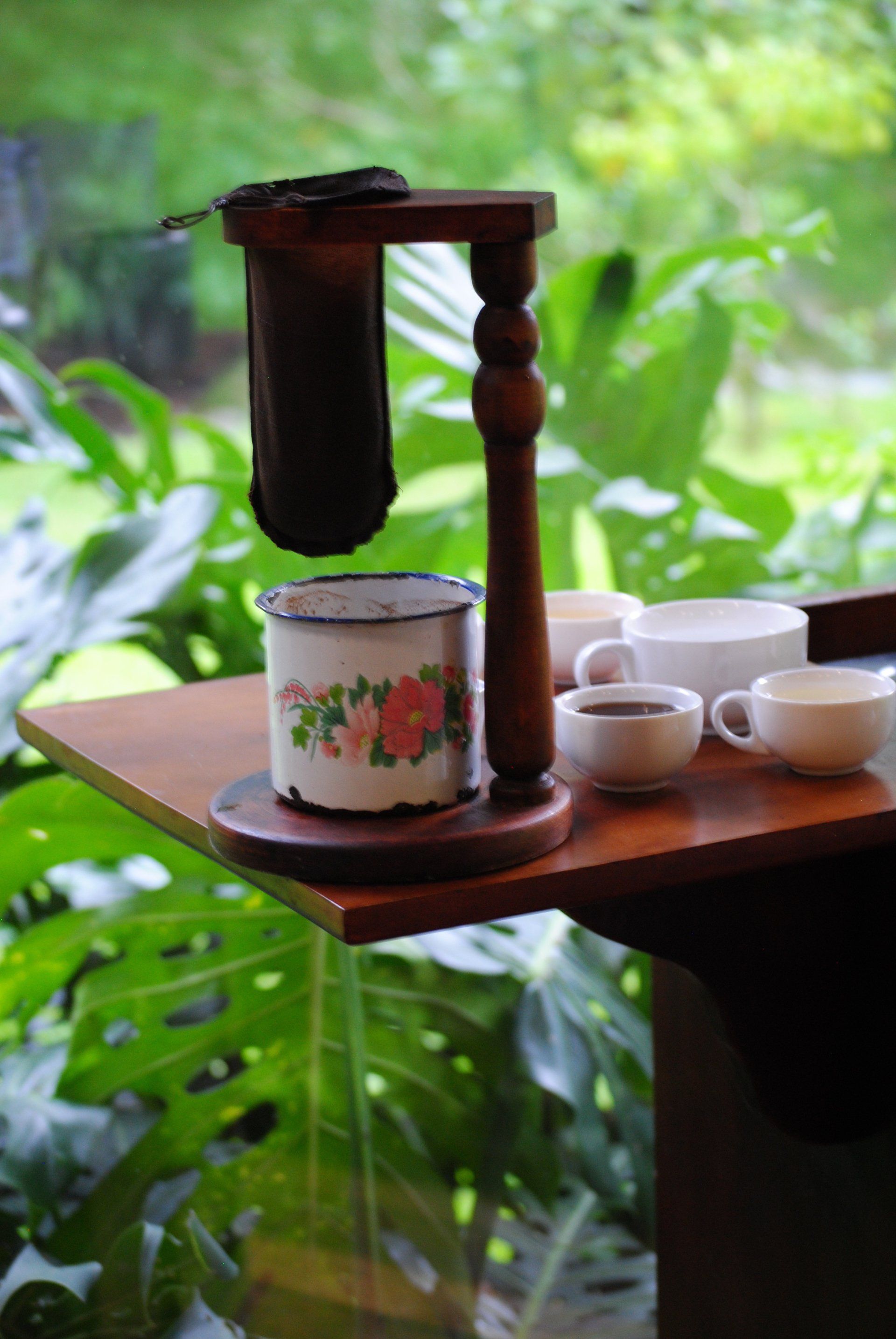 A coffee maker is sitting on a wooden table next to a cup of coffee.