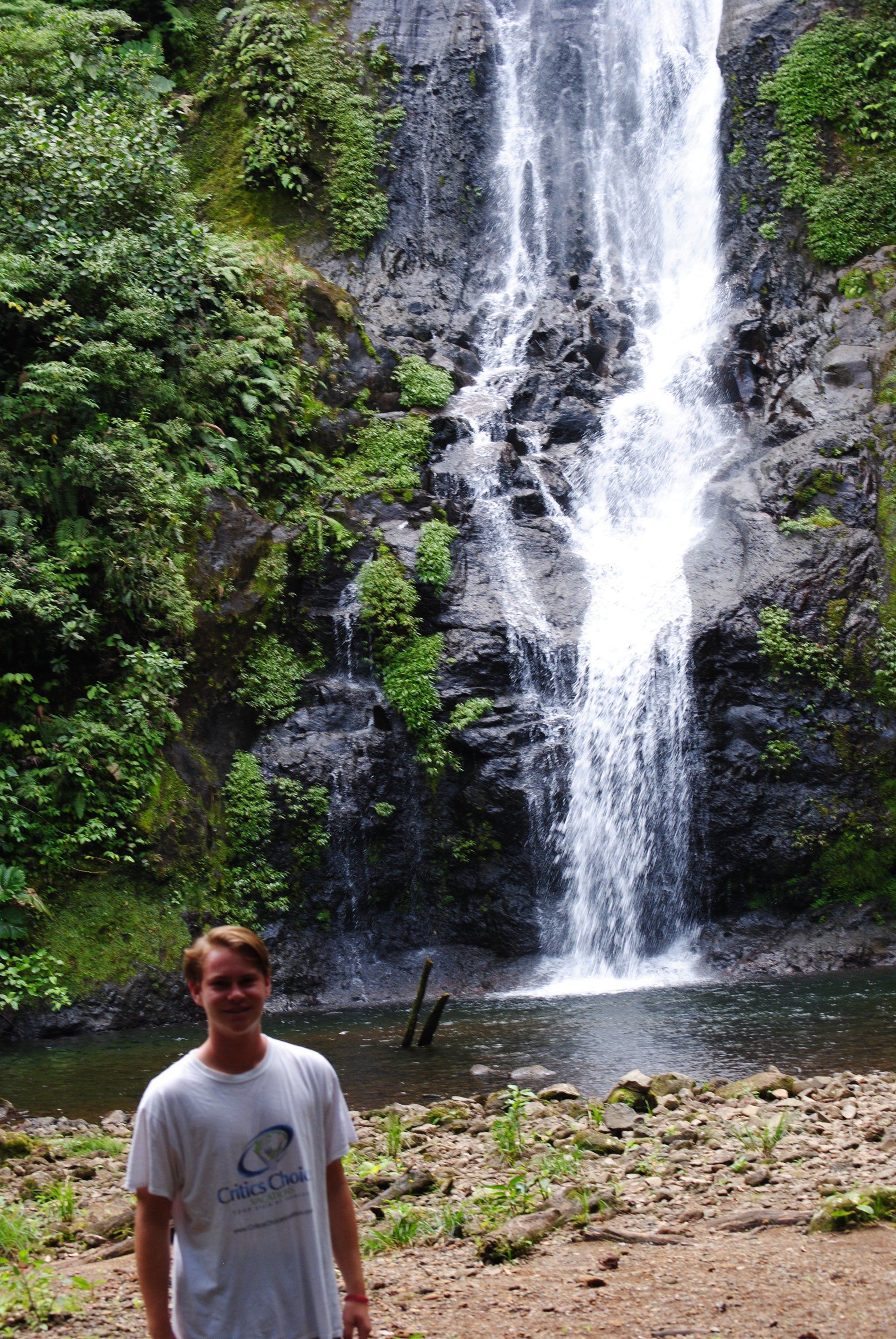 A man is standing in front of a waterfall in the woods.