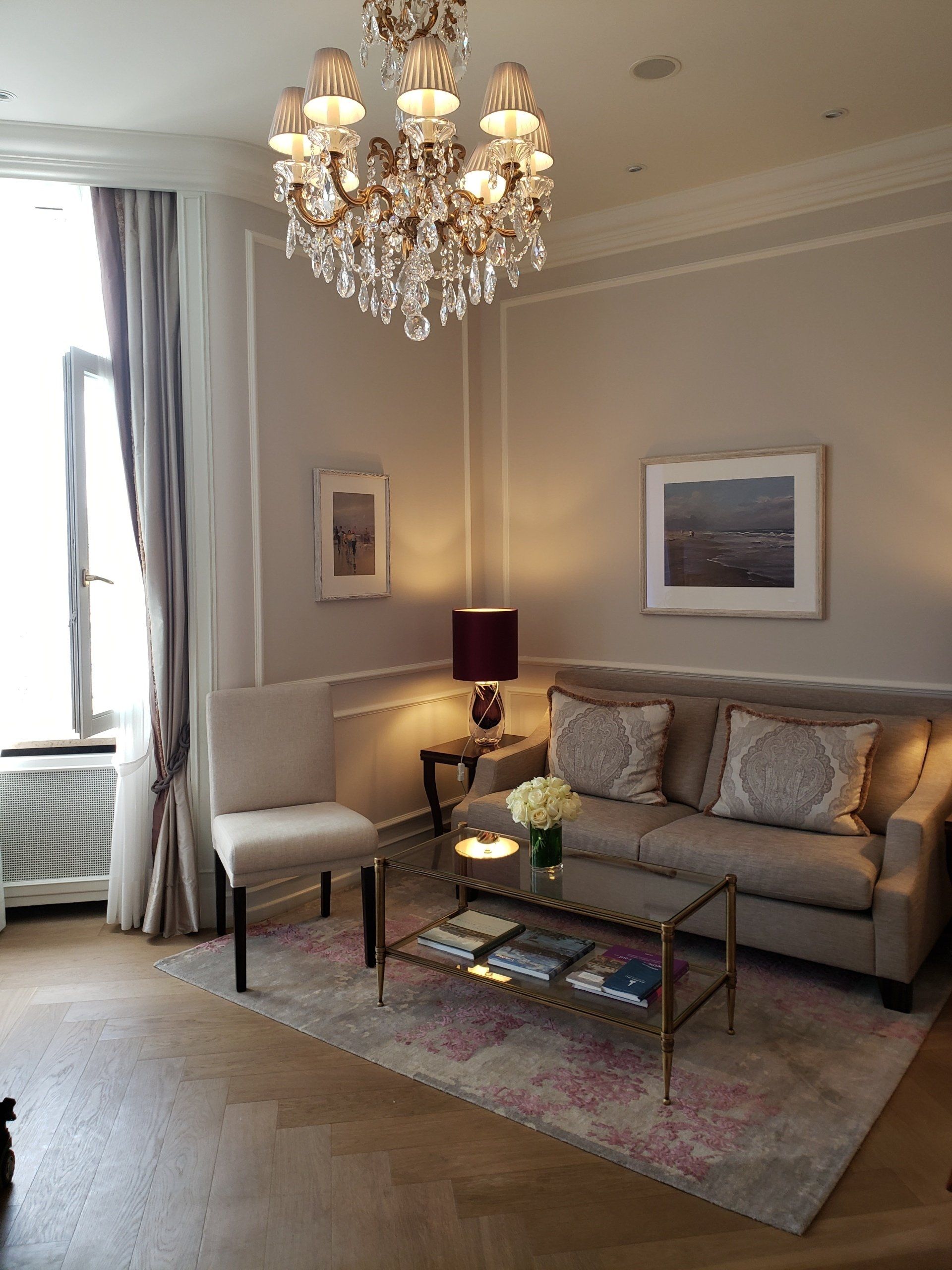 A living room with a couch , chair , coffee table and chandelier.