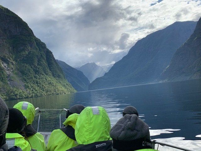 A group of people are looking out over a lake surrounded by mountains.