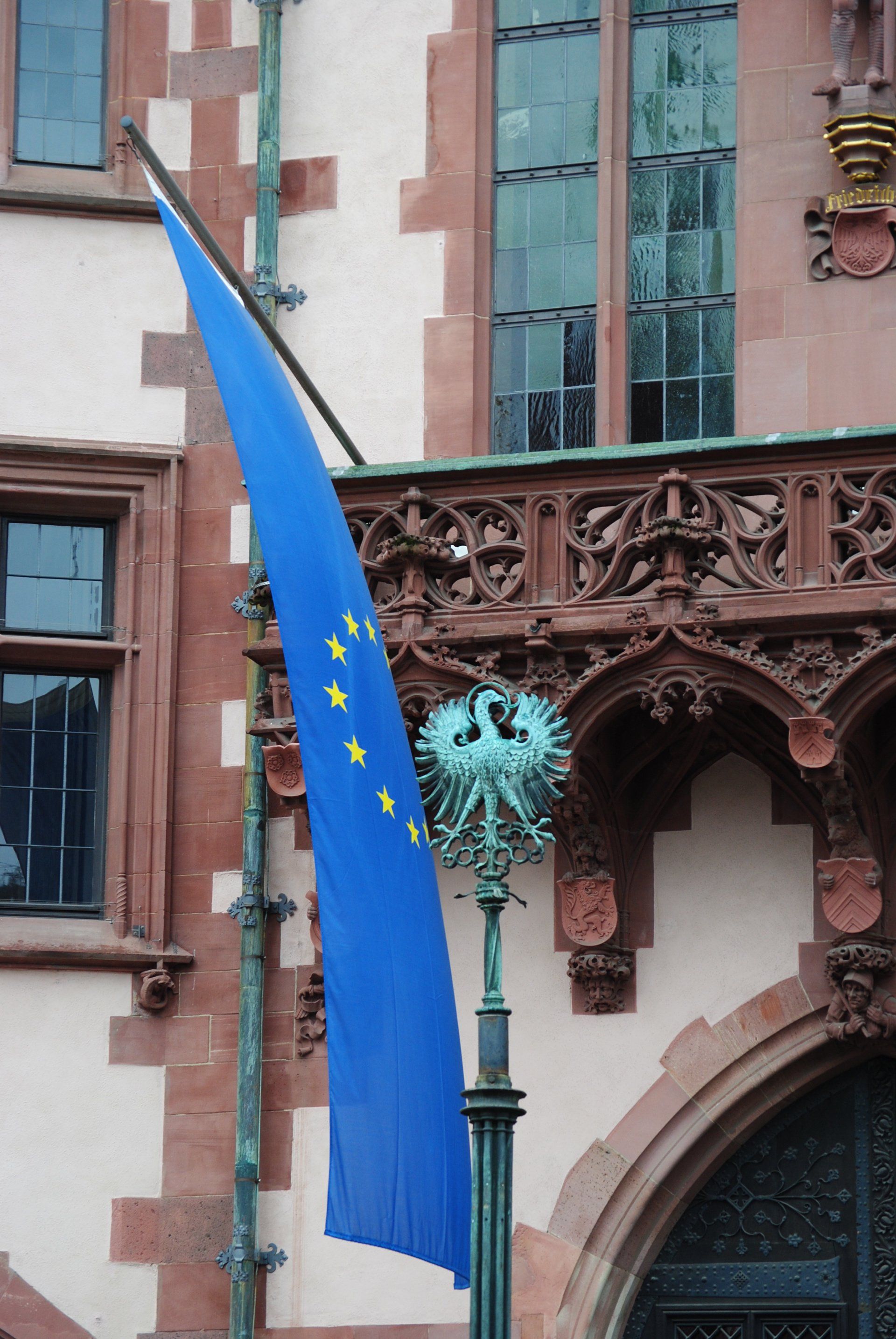 A blue flag with yellow stars is flying in front of a building