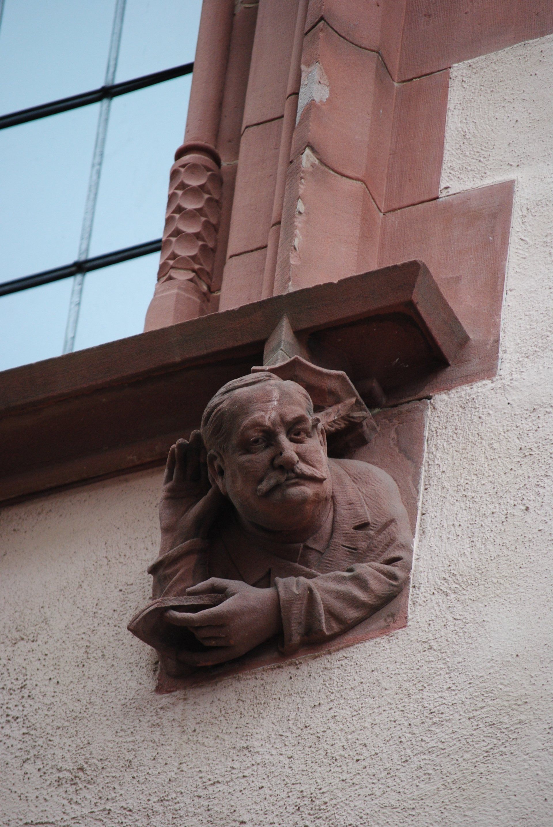 A statue of a man with a mustache is on the side of a building.