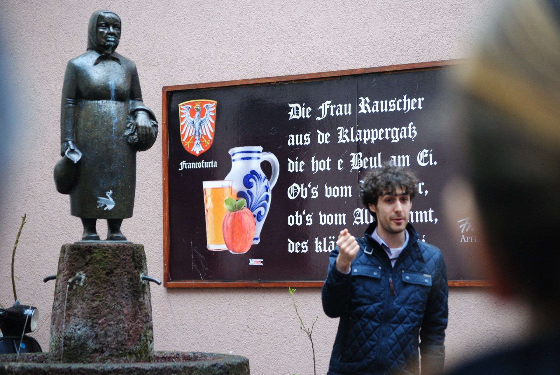 A man stands in front of a statue of a woman holding a pitcher
