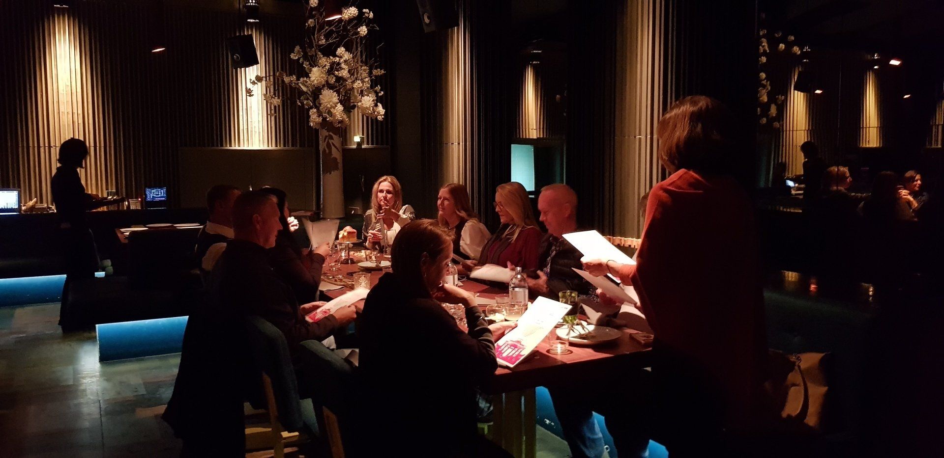 A group of people are sitting at a table in a dark room.