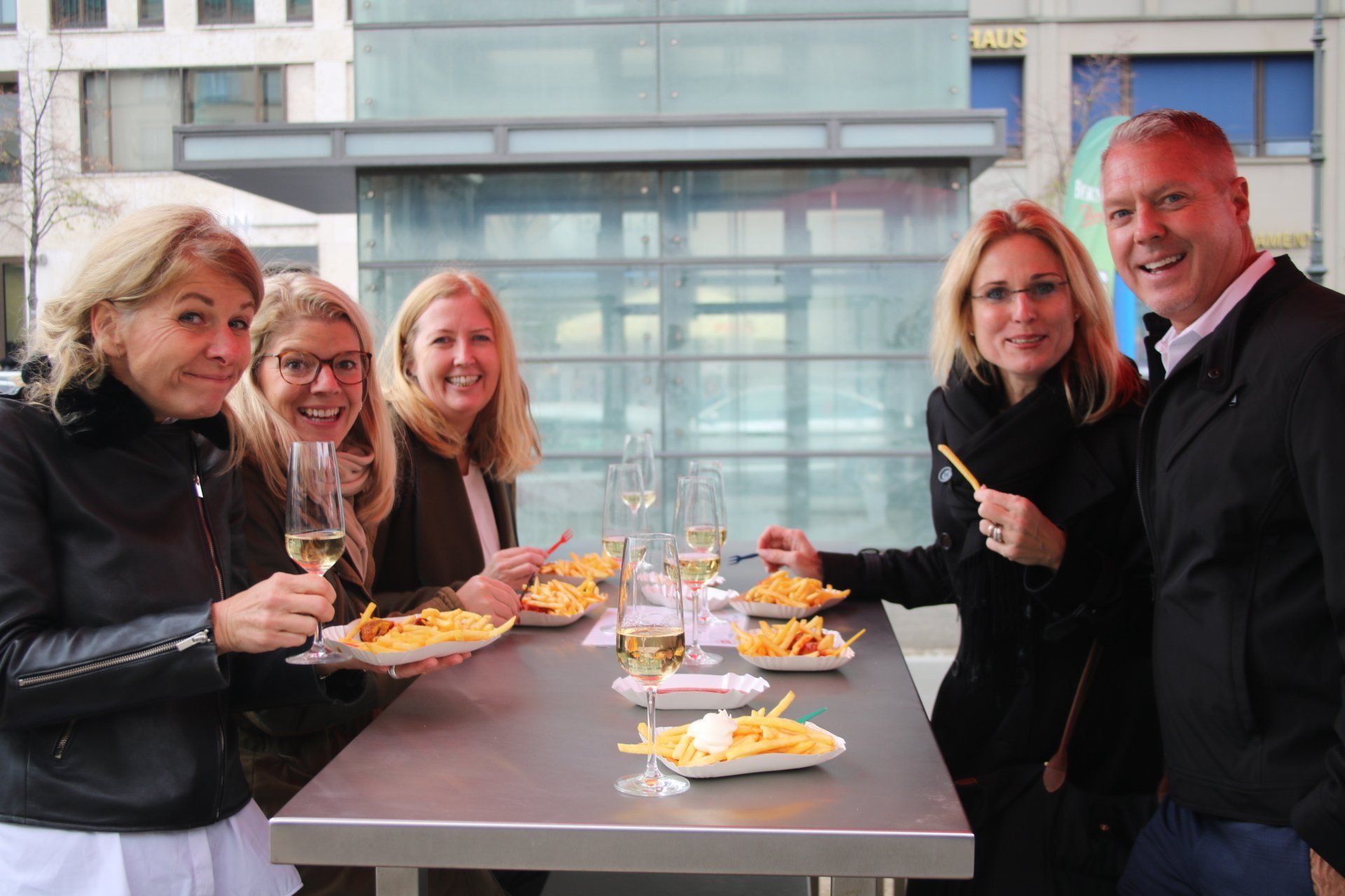 A group of people are sitting at a table eating french fries and drinking wine.
